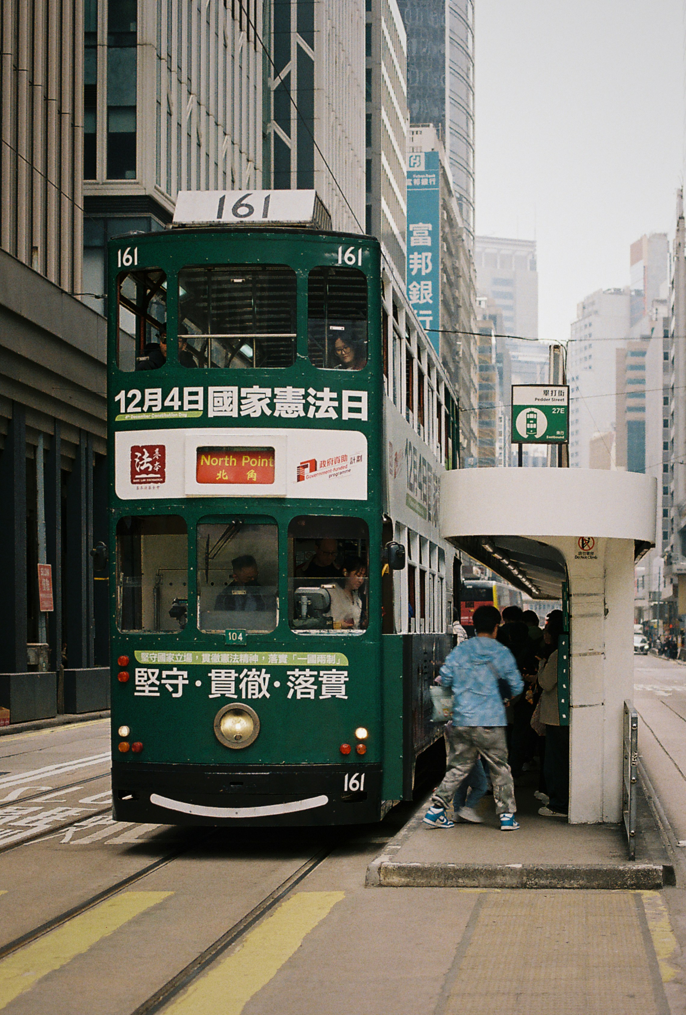 A green double-decker tram stops at a street station.