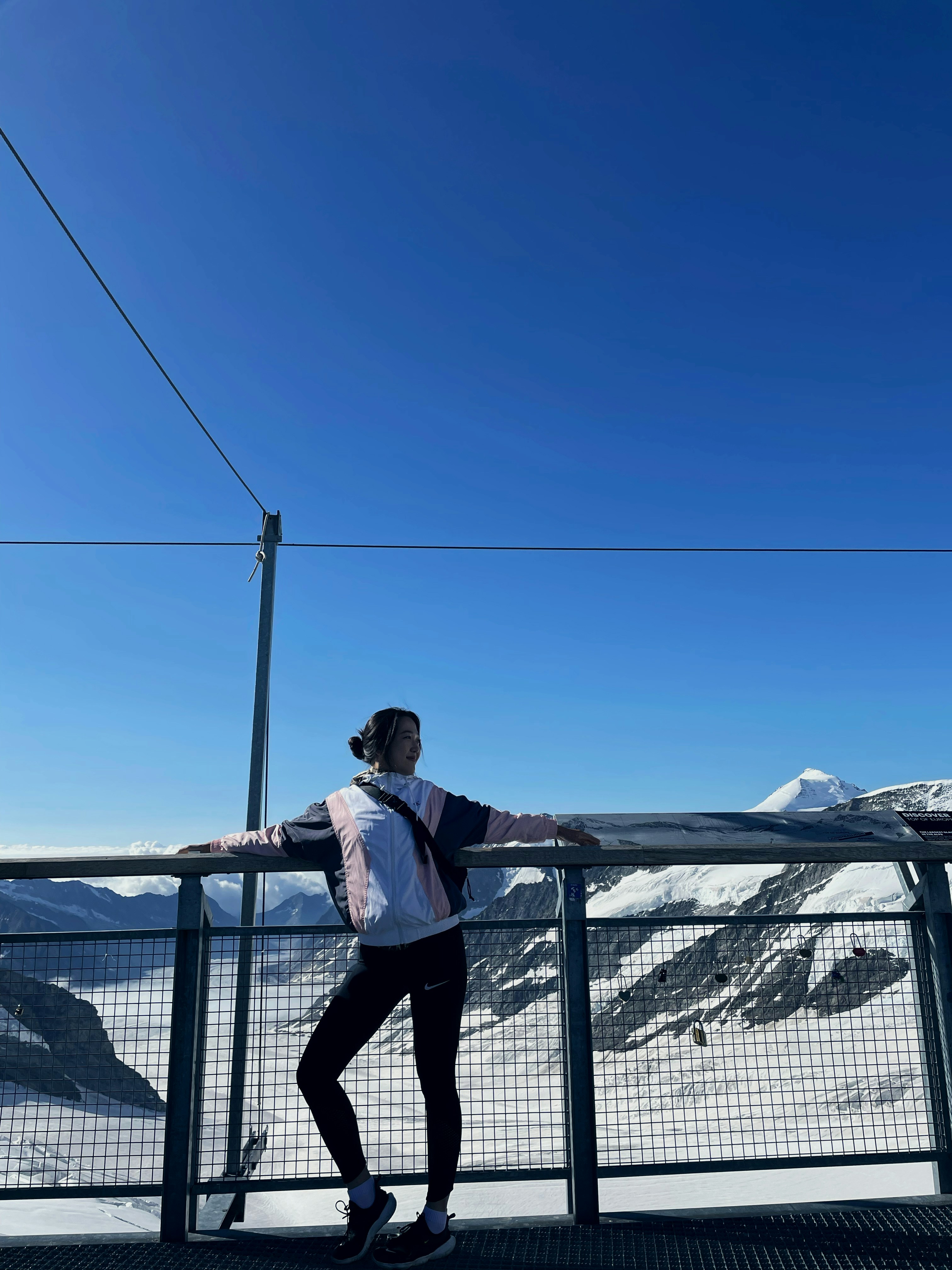 Woman stands on a platform overlooking snow-capped mountains.