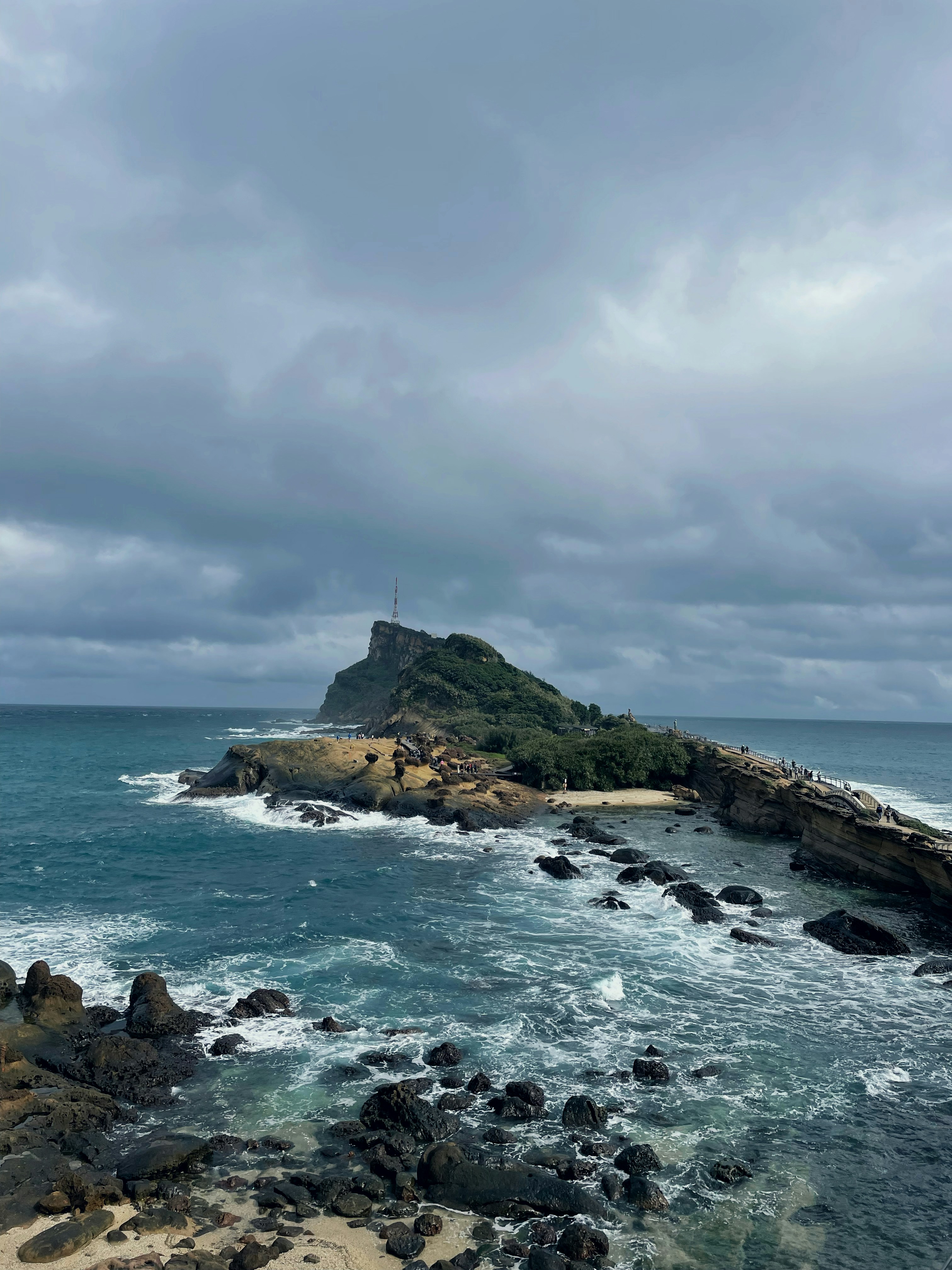 Waves crash on the rocky coast under a cloudy sky.