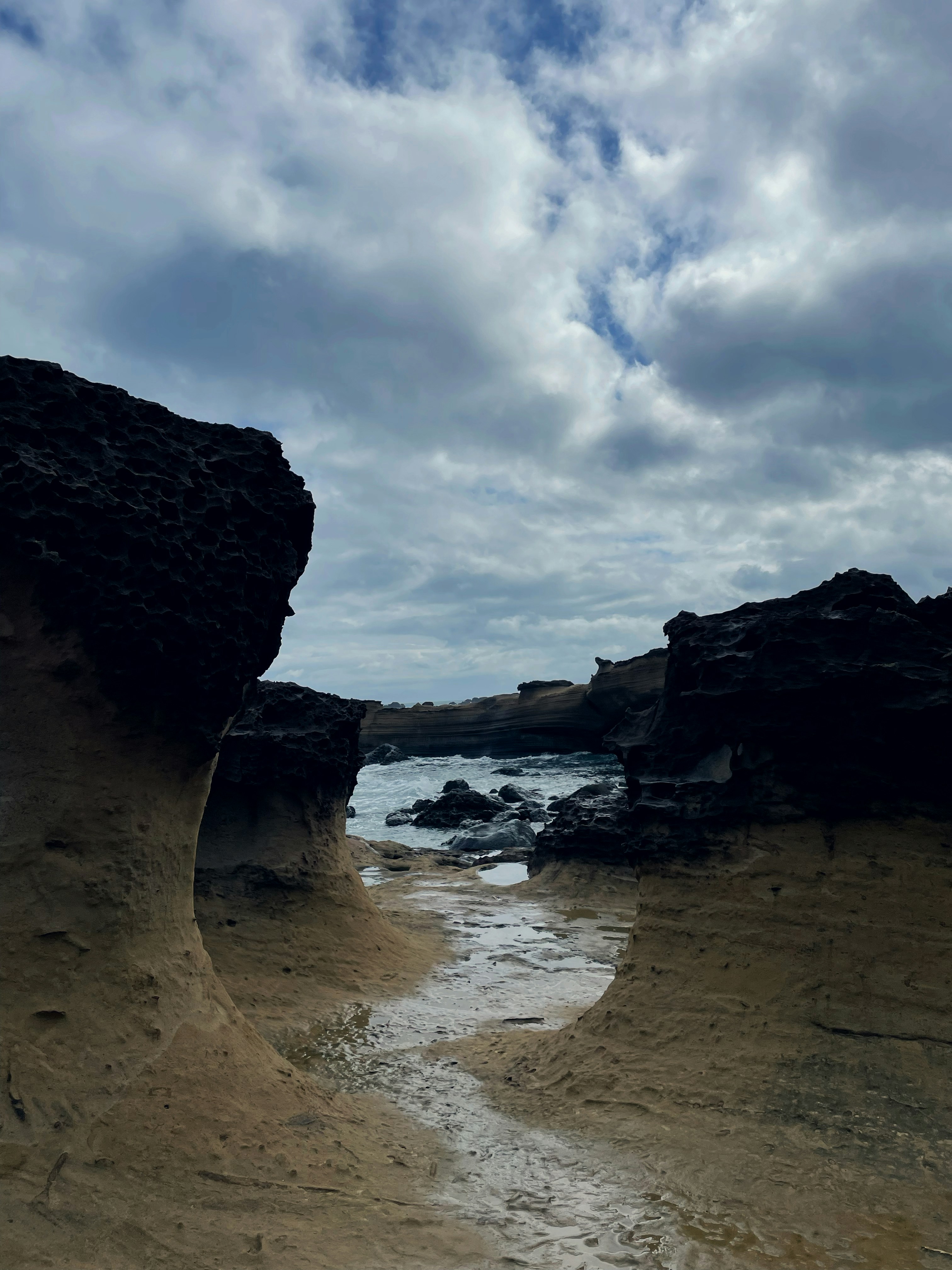 Rocky coastline meets ocean under cloudy skies.