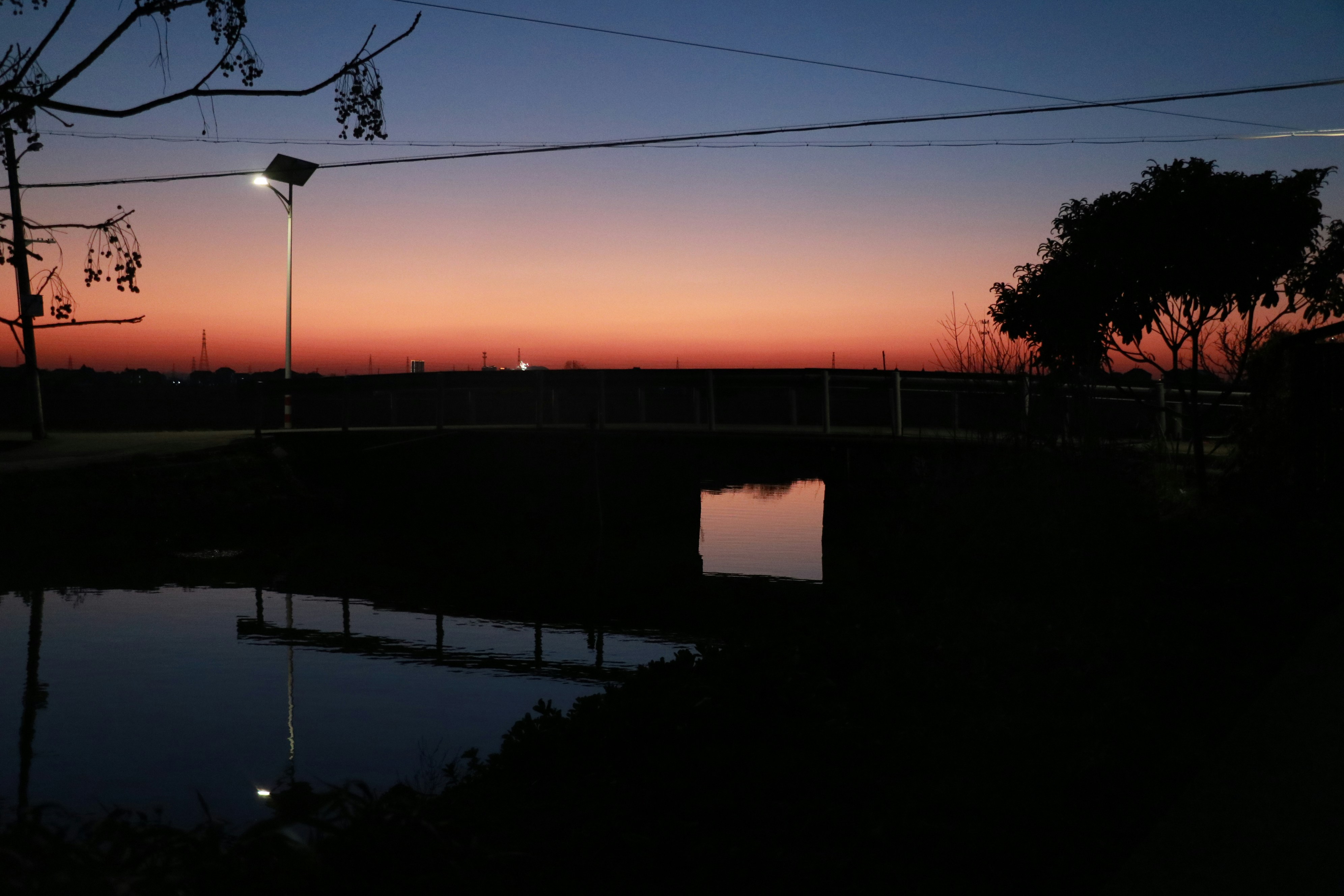 The sunset paints the sky over a dark pond.