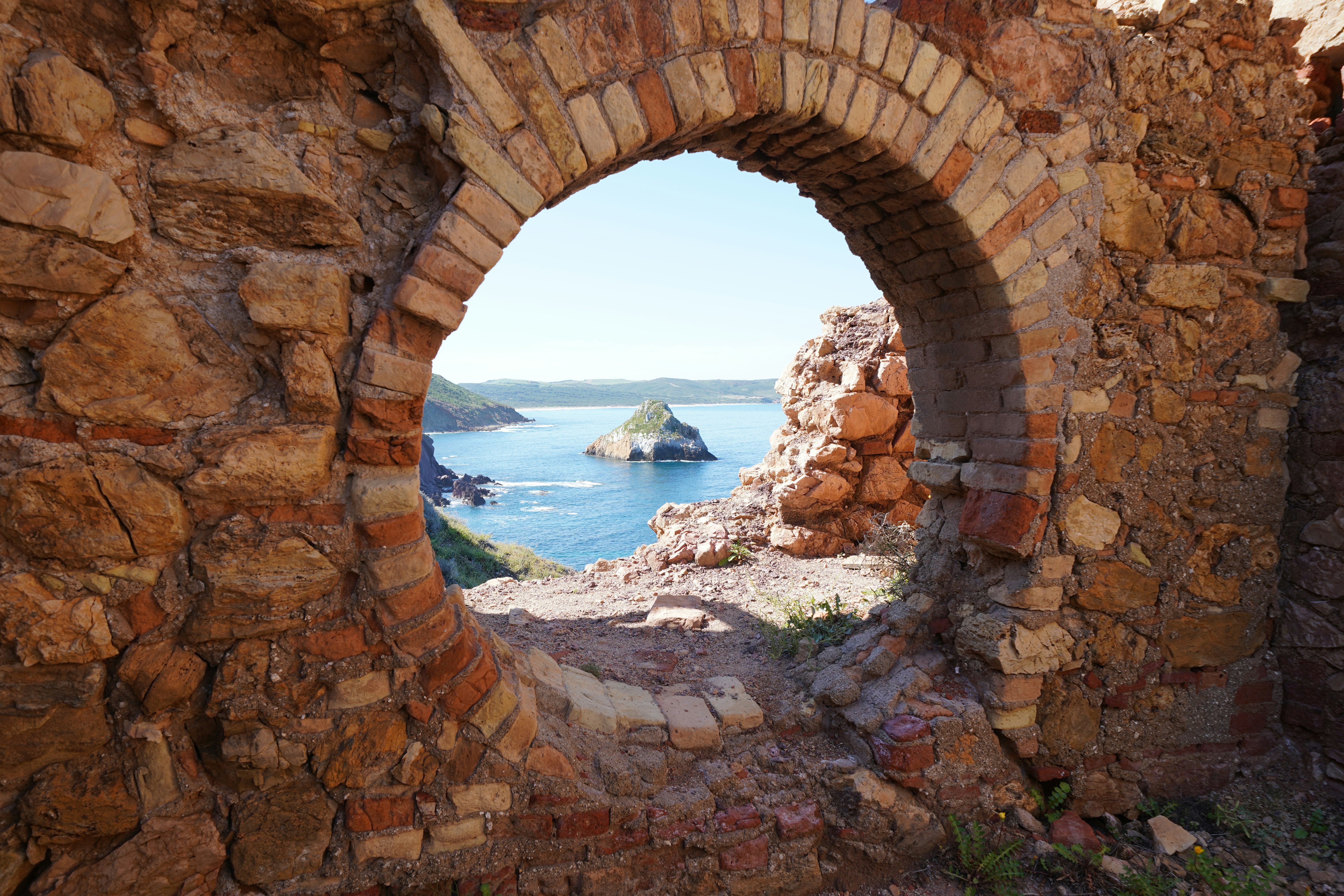 Une fenêtre cintrée encadre un paysage côtier.