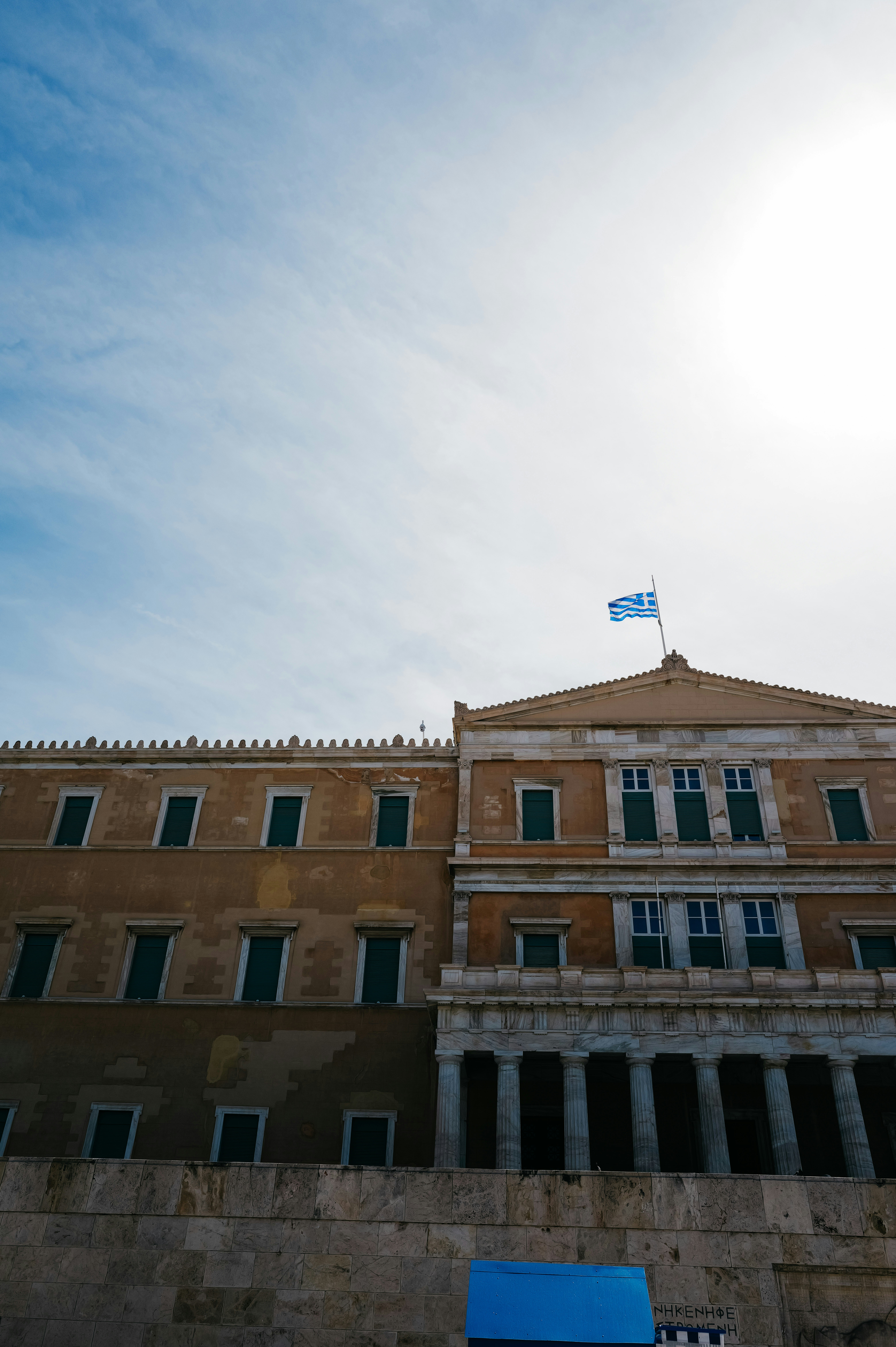 Greek parliament building with flag under a sunny sky.