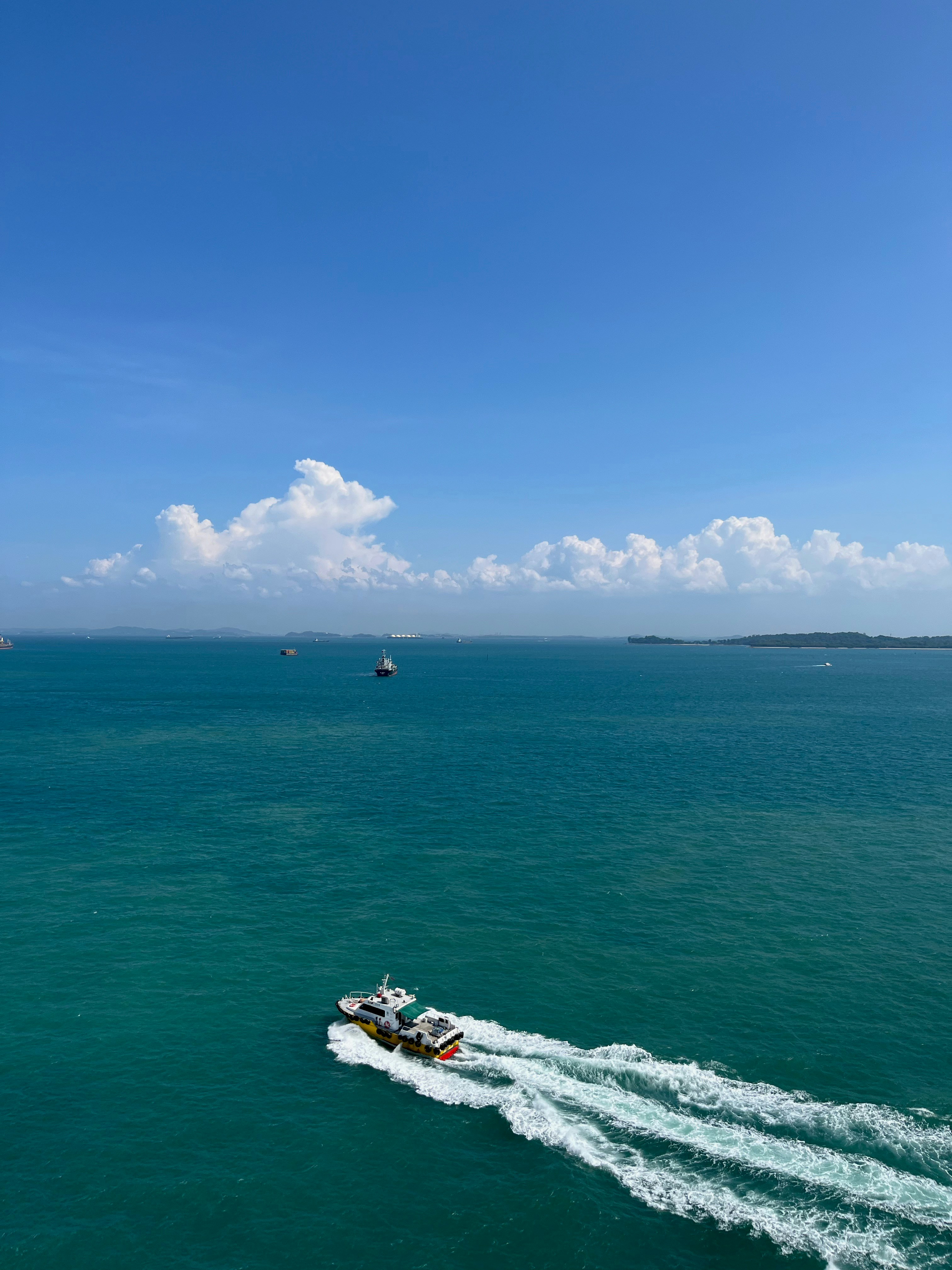 Boats sail across the turquoise ocean under the sunny sky.