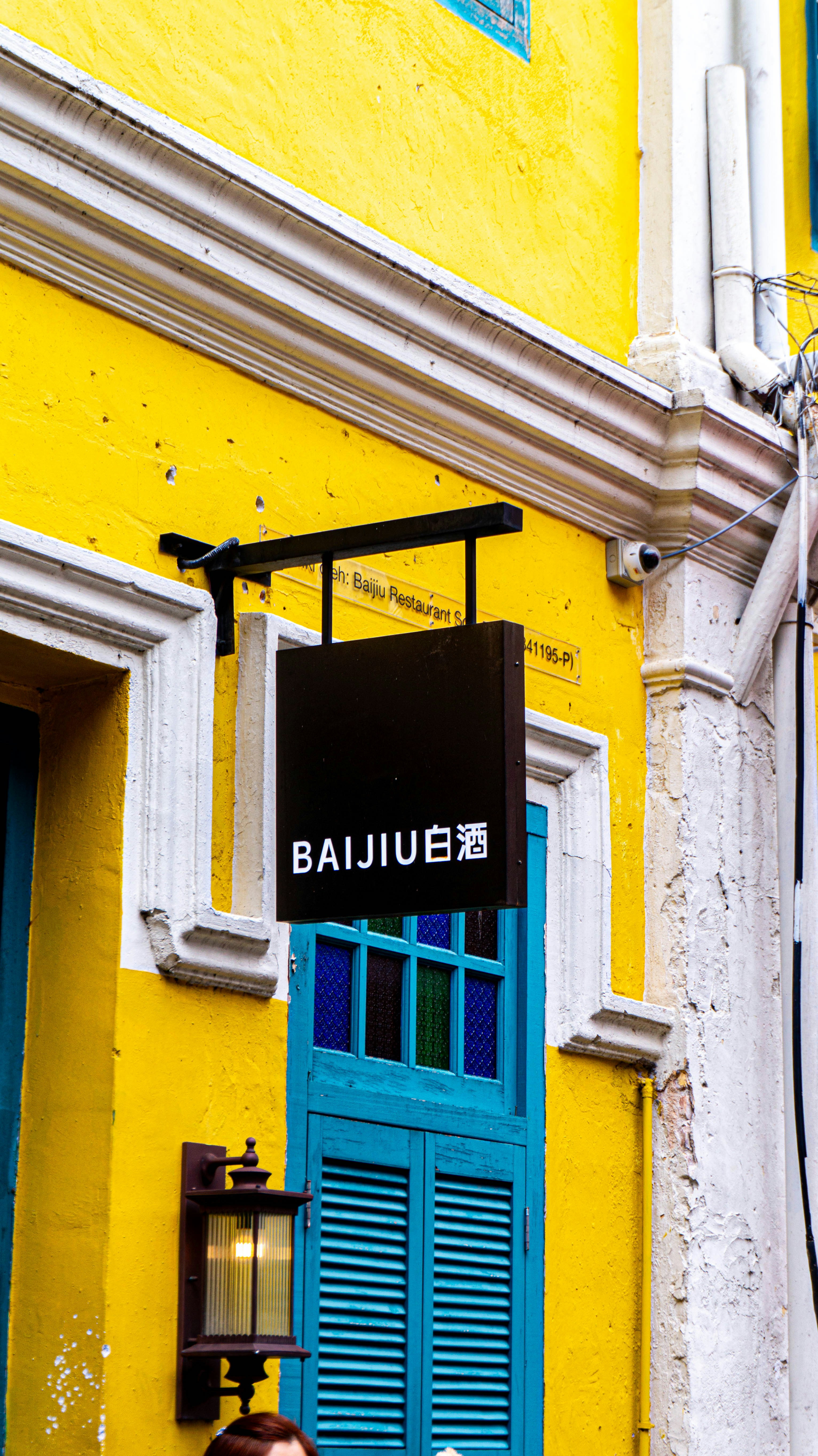 A restaurant sign reads "baijiu" on a bright yellow building.