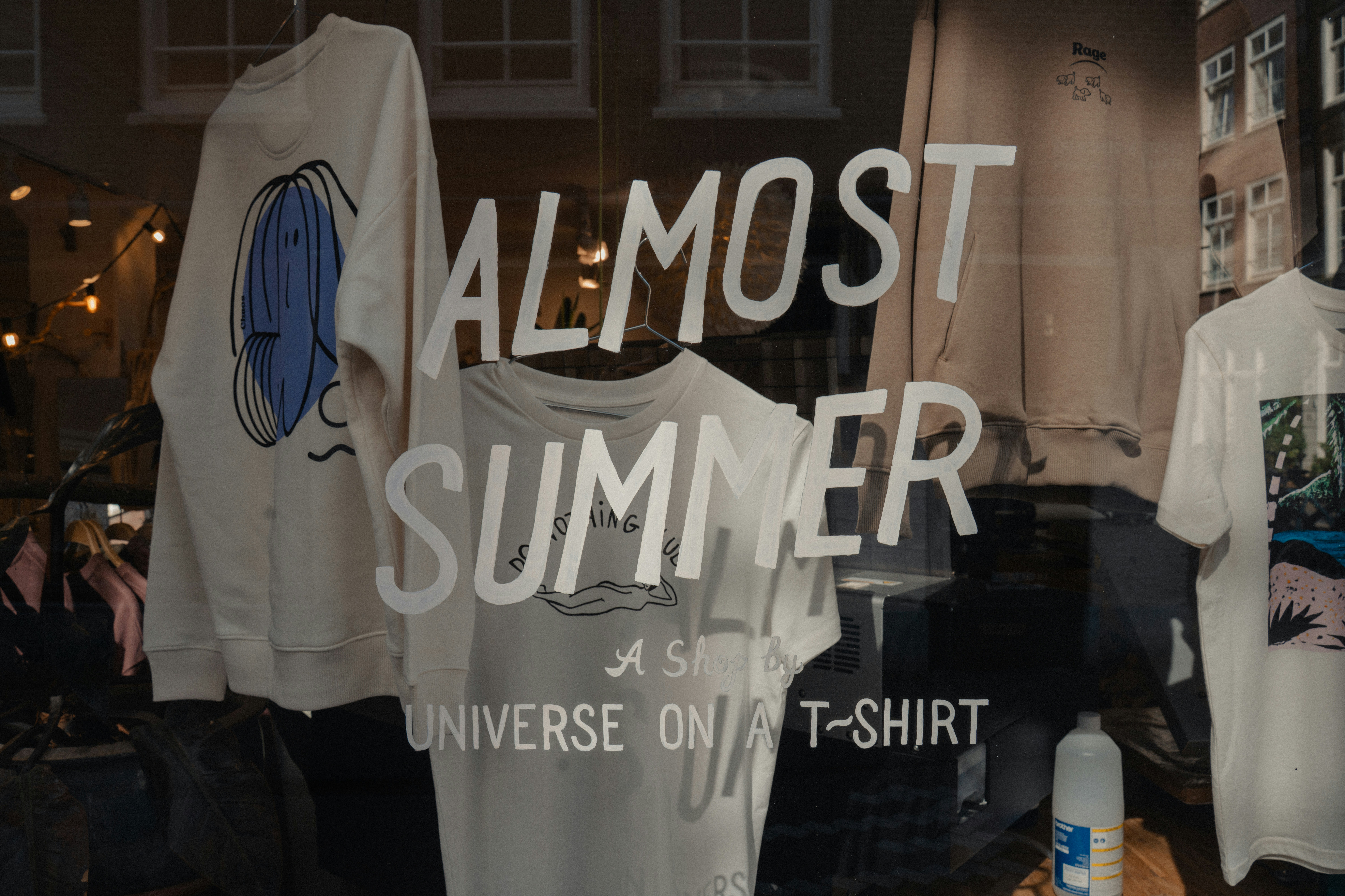 Shop window displays "almost summer" t-shirts.