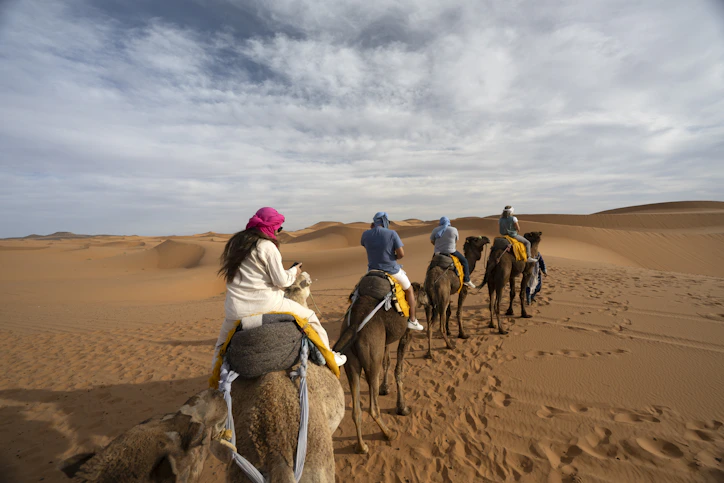 People ride camels across a desert landscape.