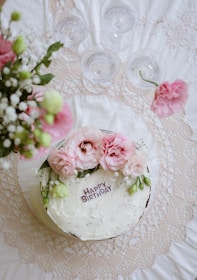 A birthday cake is surrounded by flowers and glassware.