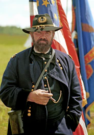 A civil war reenactor poses with flags and a cigar.