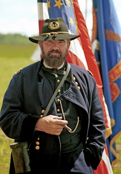 A civil war reenactor poses with flags and a cigar.