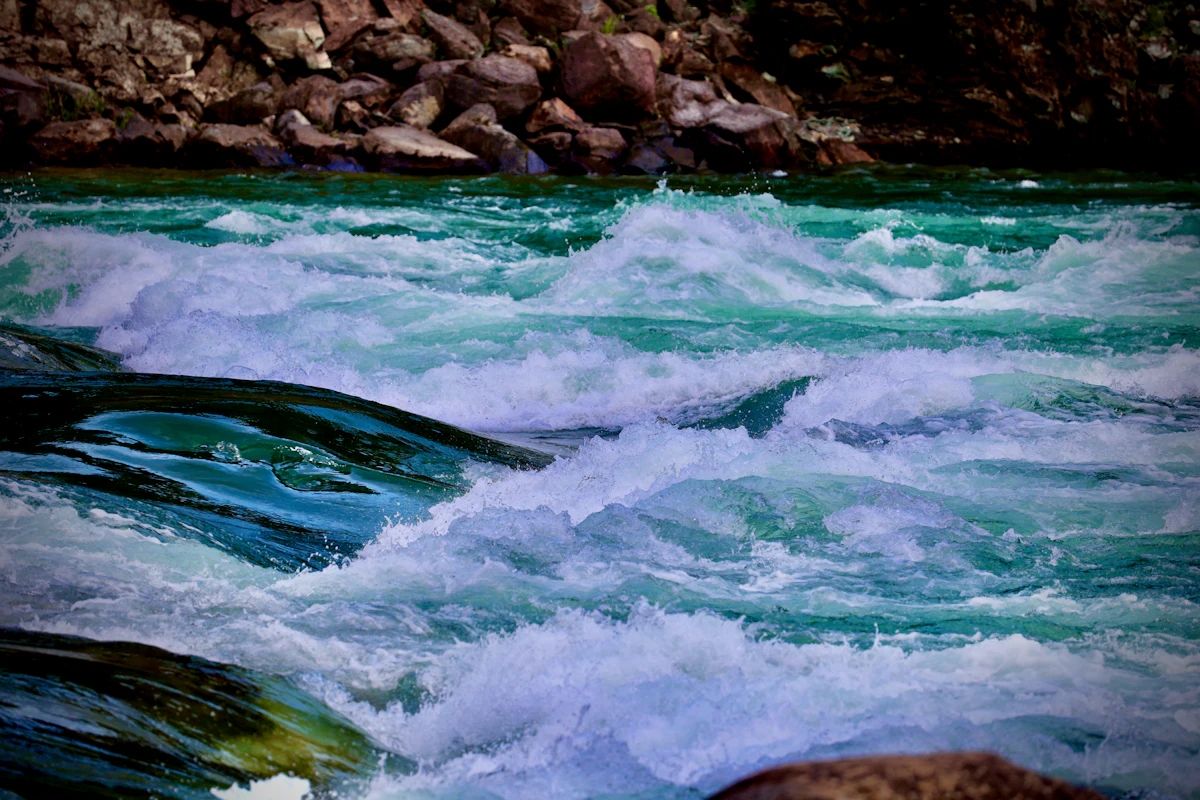 Whitewater rapids in a main-stem river with rocky bank — the high-flow conditions Texas Tuff Rock Bags armor against