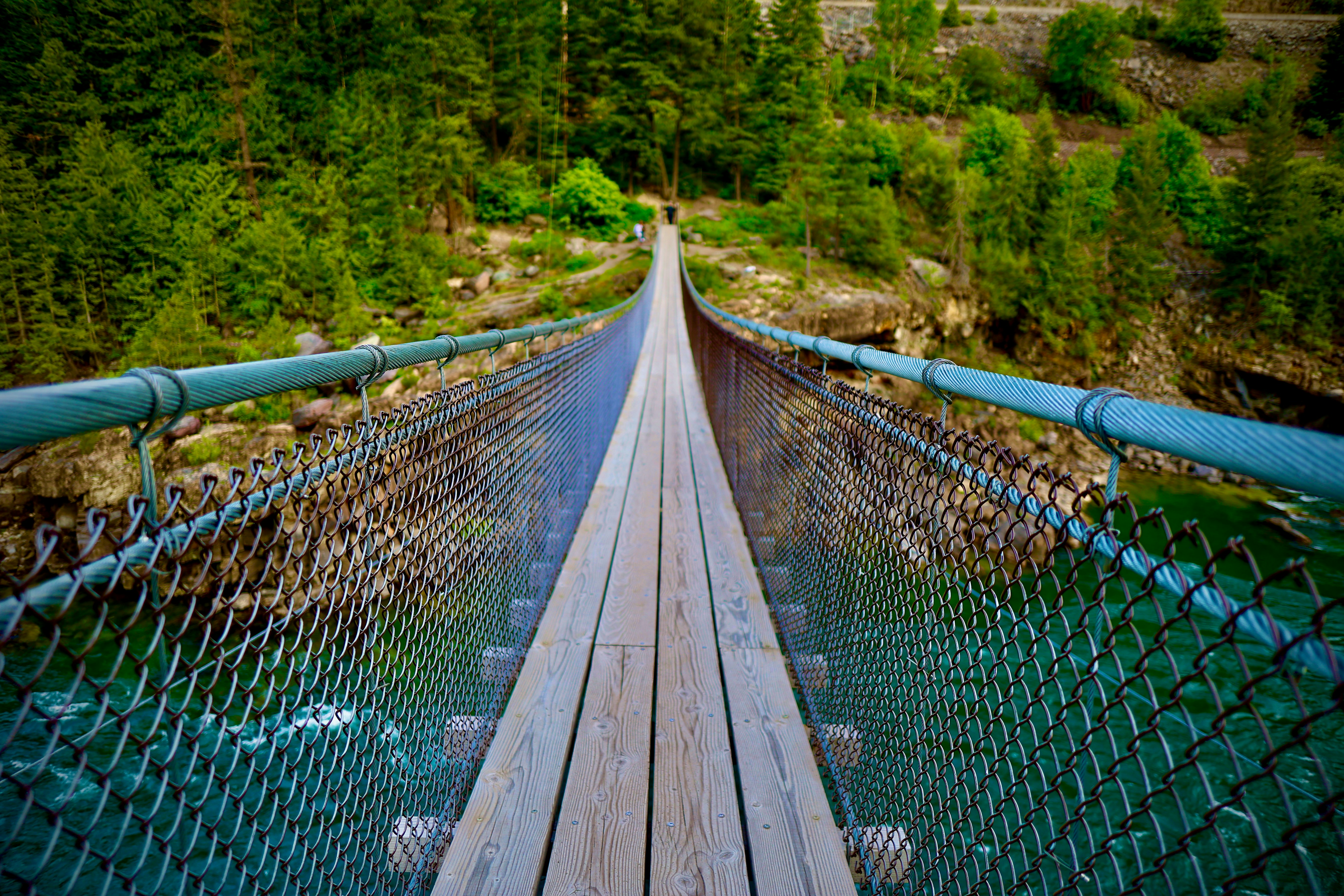A suspension bridge spans a beautiful, green river.