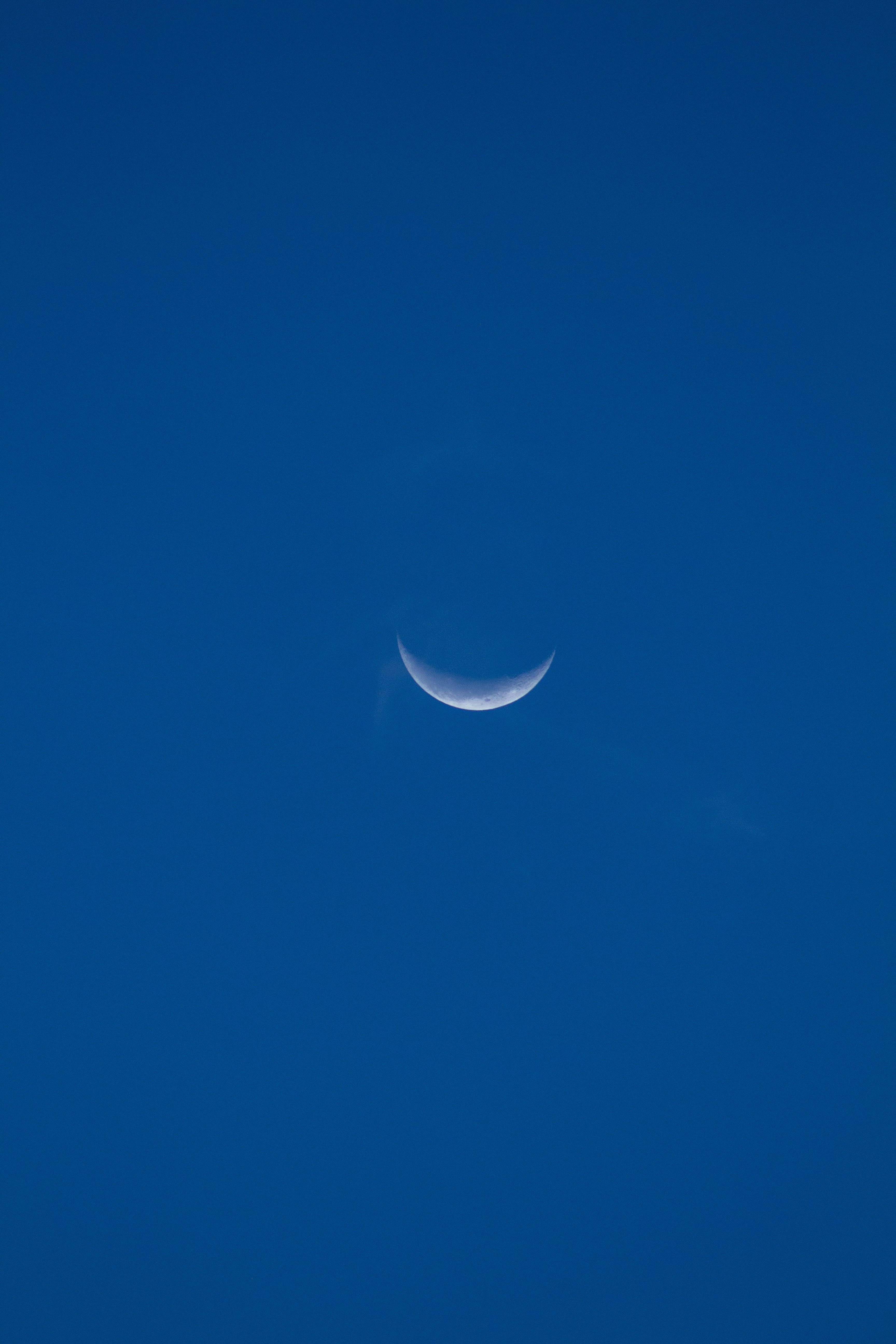 Crescent moon shines in the clear, blue sky.