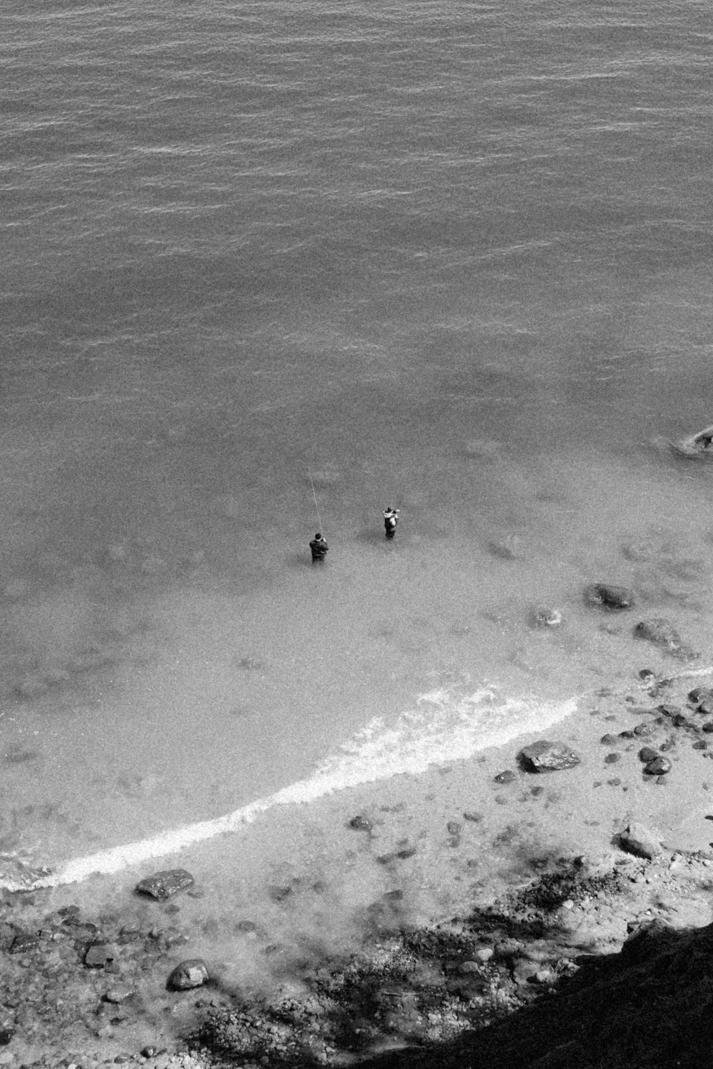 Two people stand fishing in shallow water.