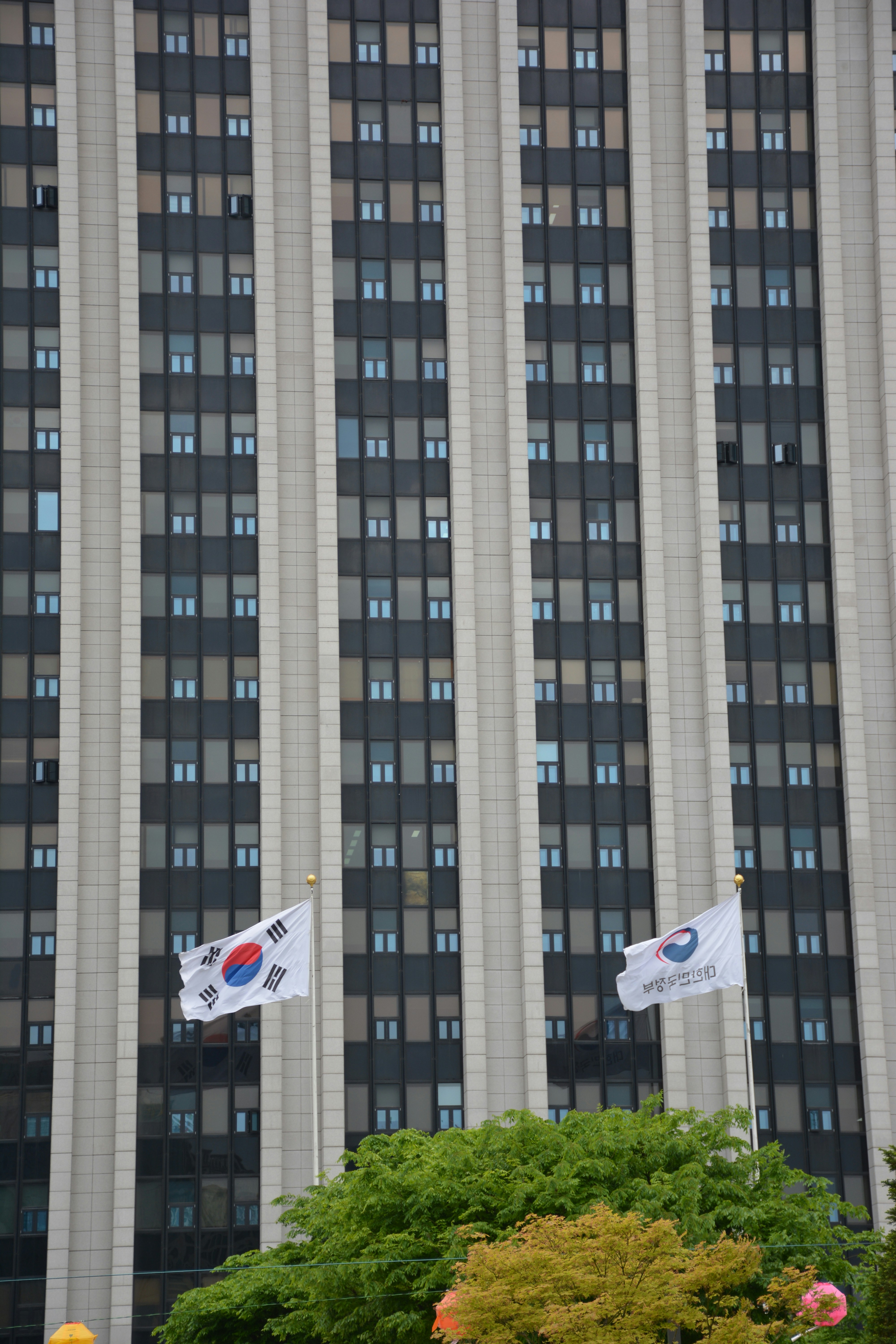 Vor einem hohen Gebäude wehen Fahnen.