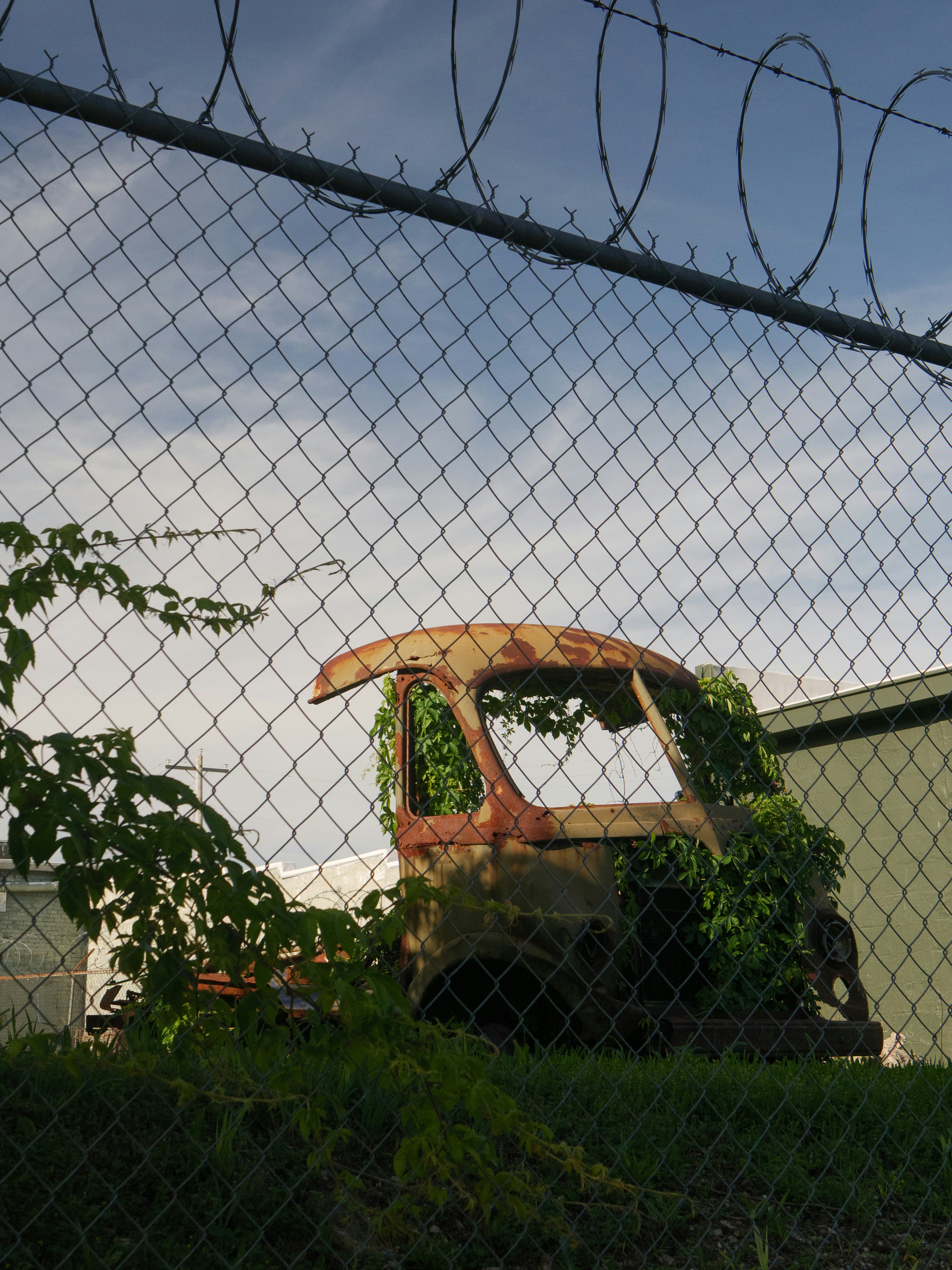 A rusty truck sits behind a barbed wire fence.
