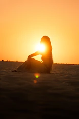 Woman's silhouette sits in golden sunset.