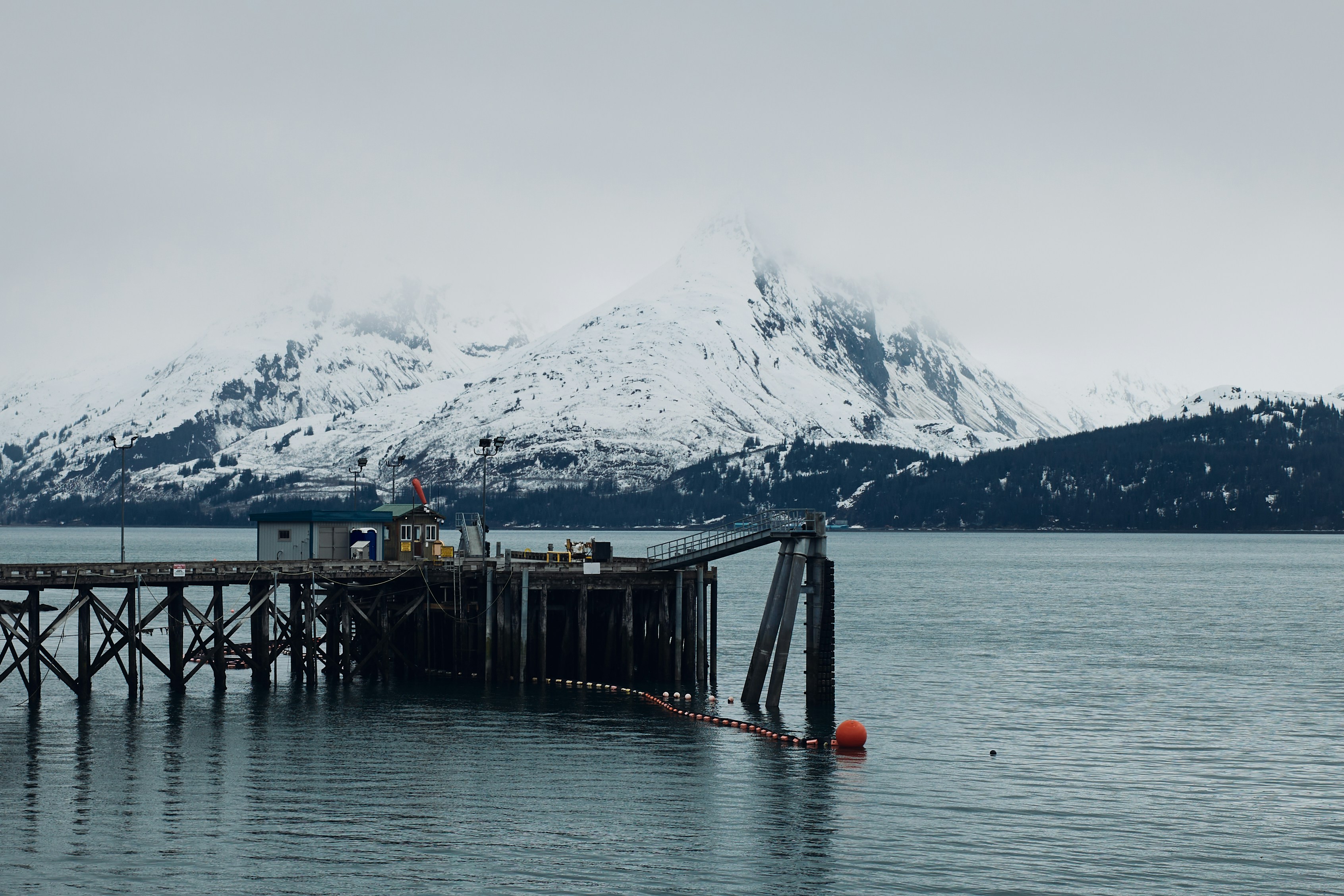A pier extends into the icy ocean, with mountains.