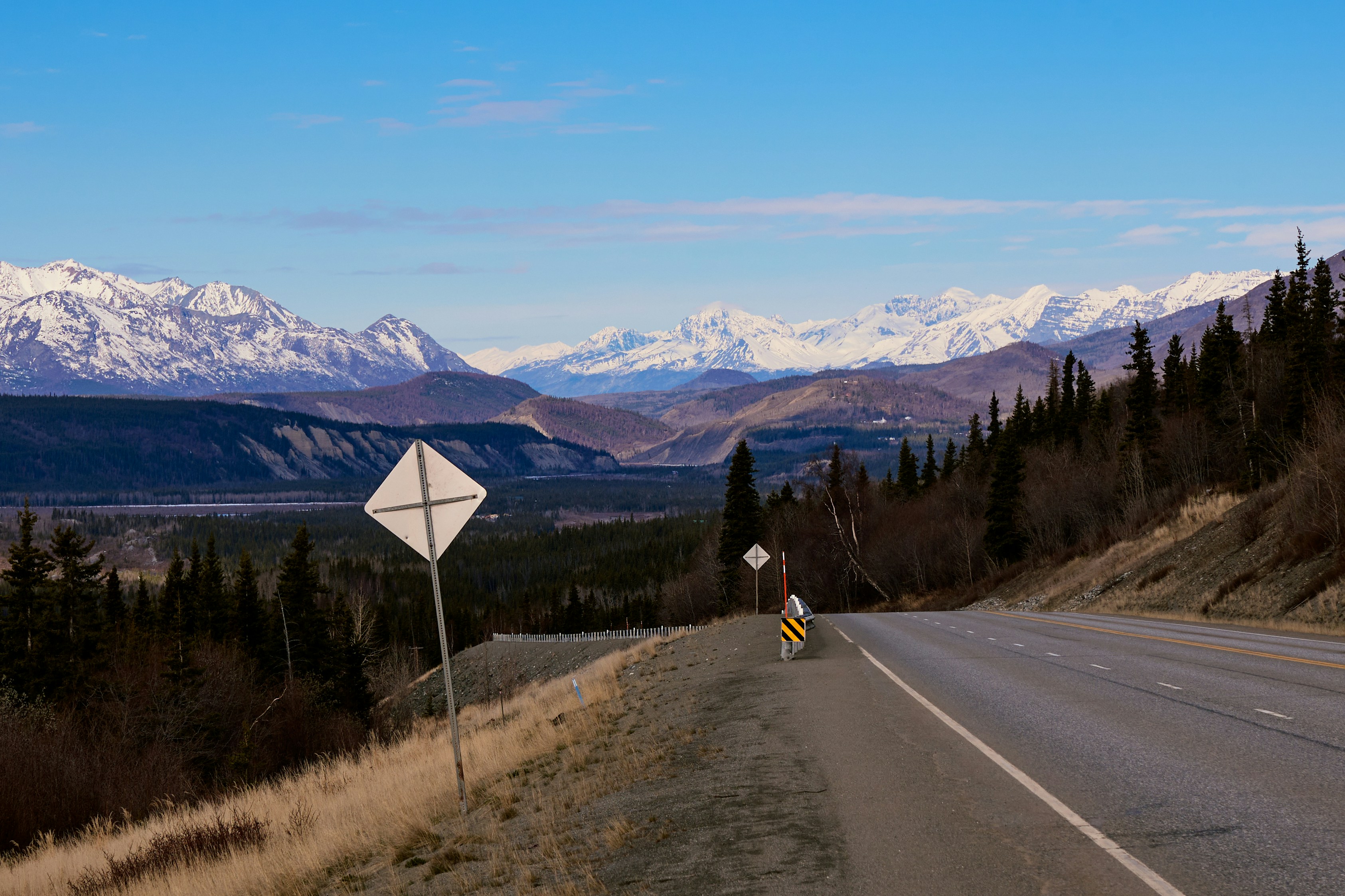 Road winds toward snow-capped mountains under blue skies.