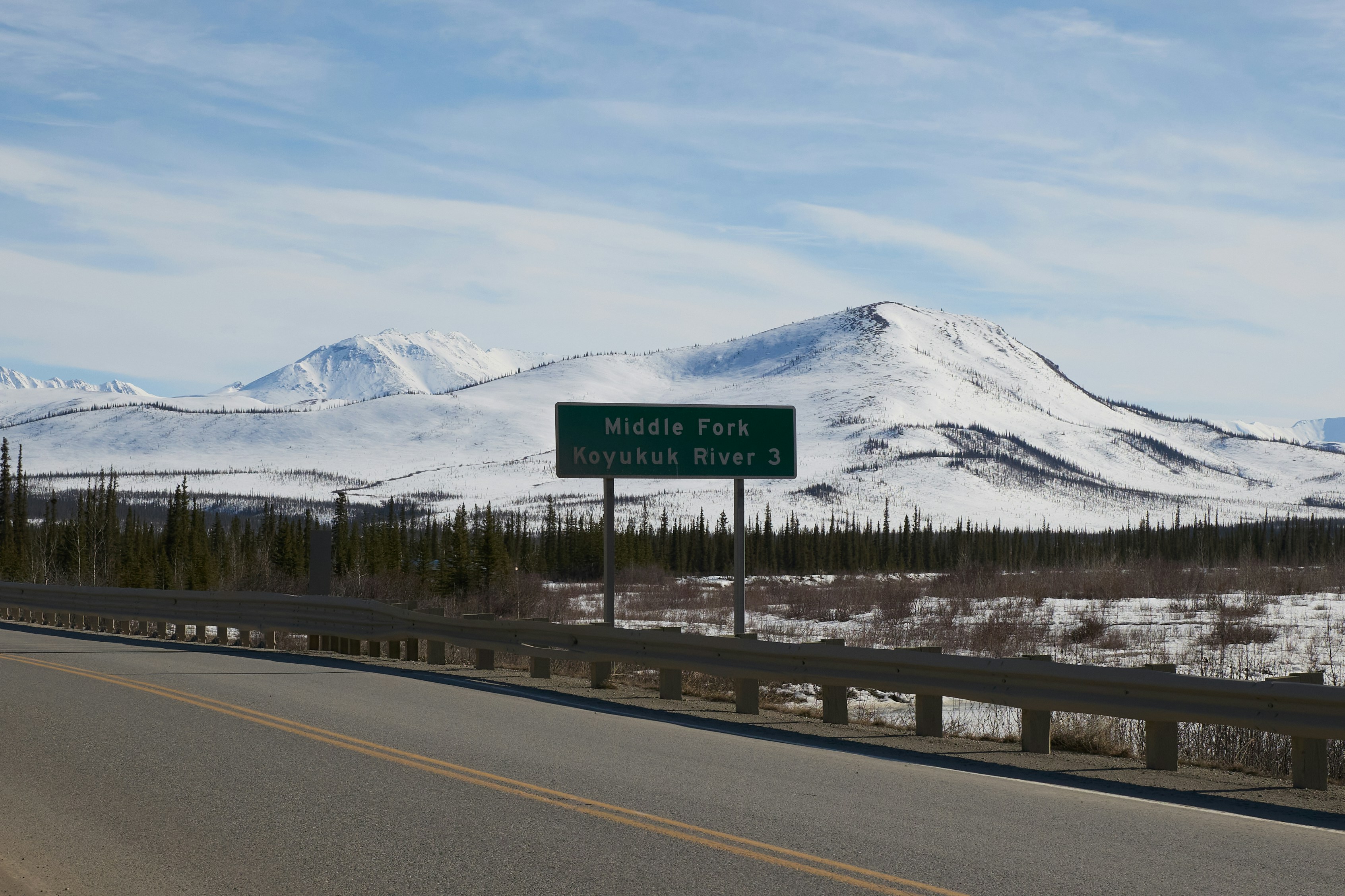 A road sign sits against snowy mountains.