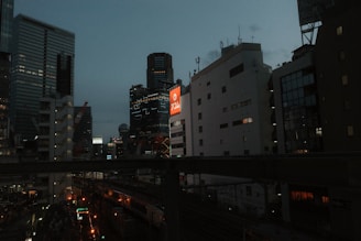 Cityscape at dusk with glowing lights and buildings.