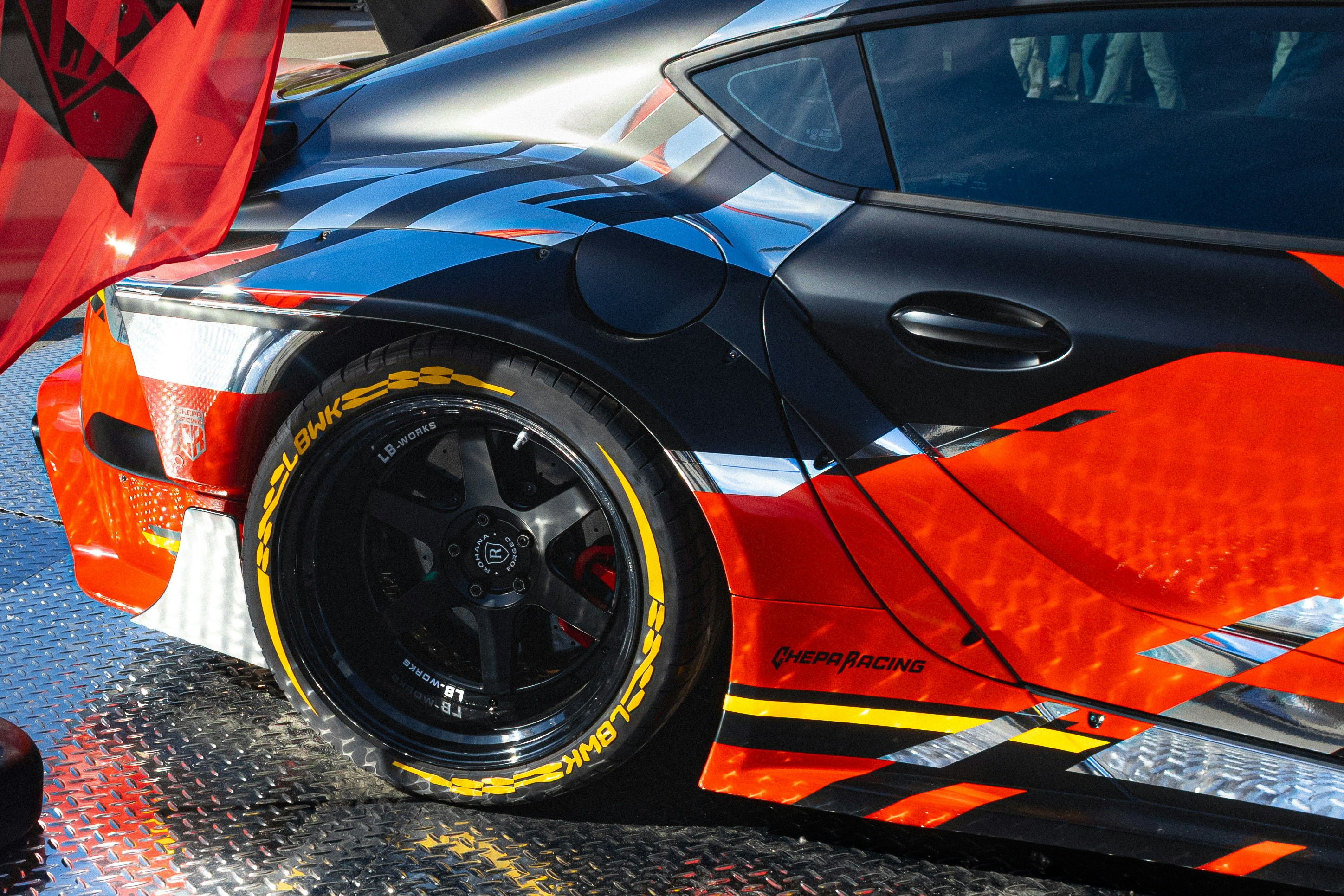 Rear quarter of a sports car covered in orange, gray and black vehicle graphics.