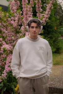 Young man poses with headphones near pink flowers.