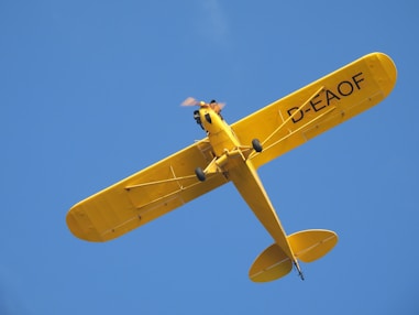 A yellow airplane flies in a clear, blue sky.