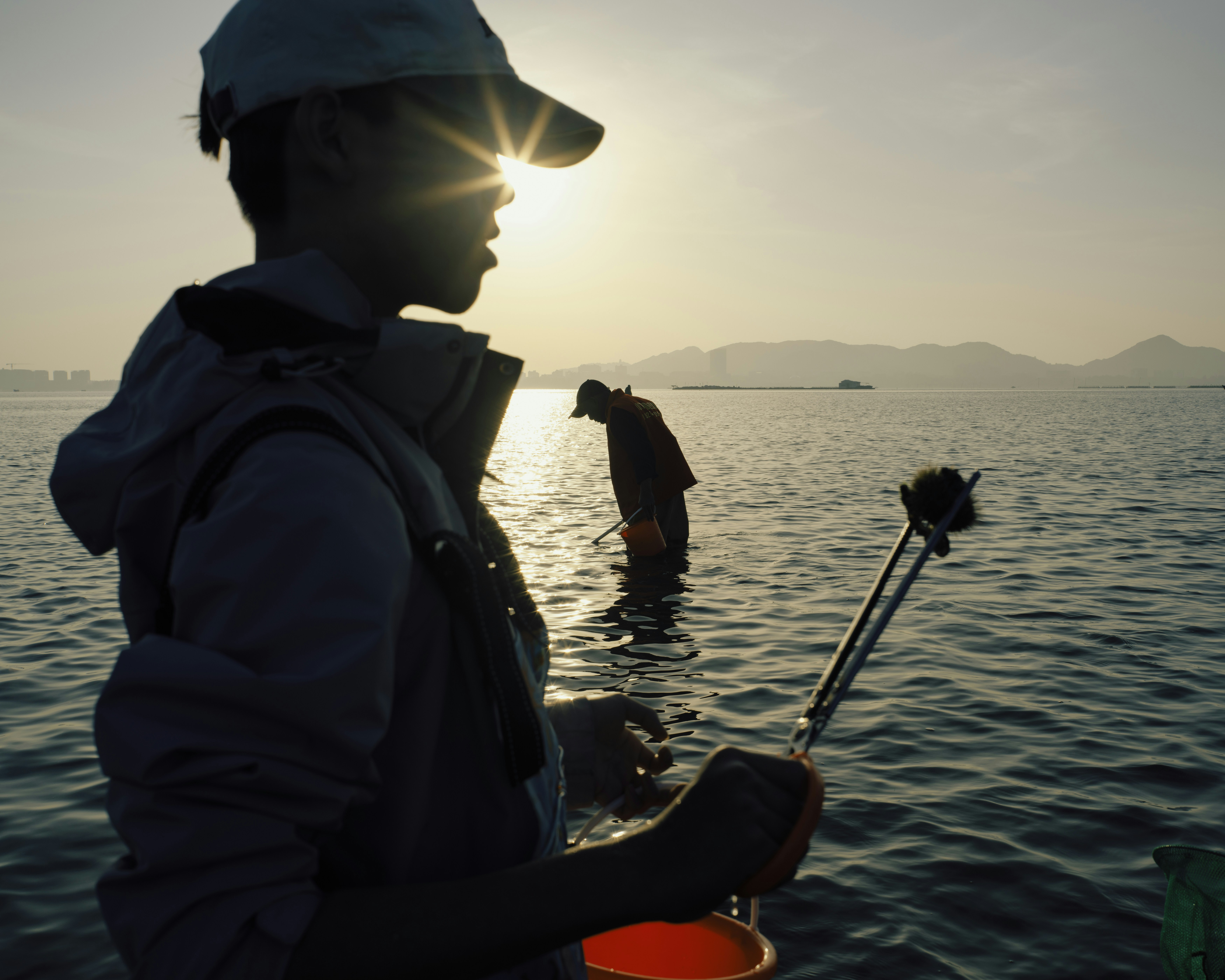 Fishermen work in the water during sunset.