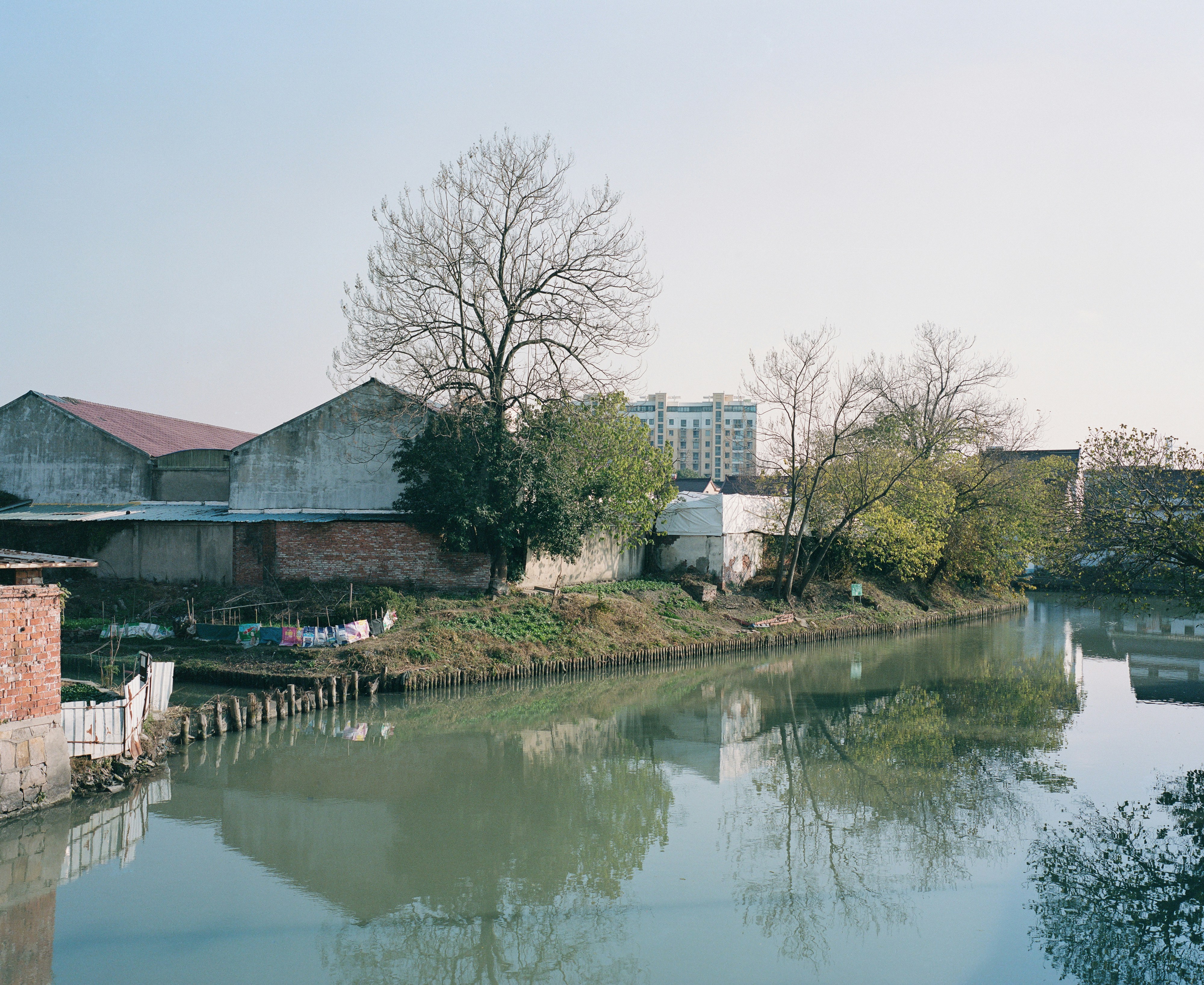 A calm river reflects trees and buildings.