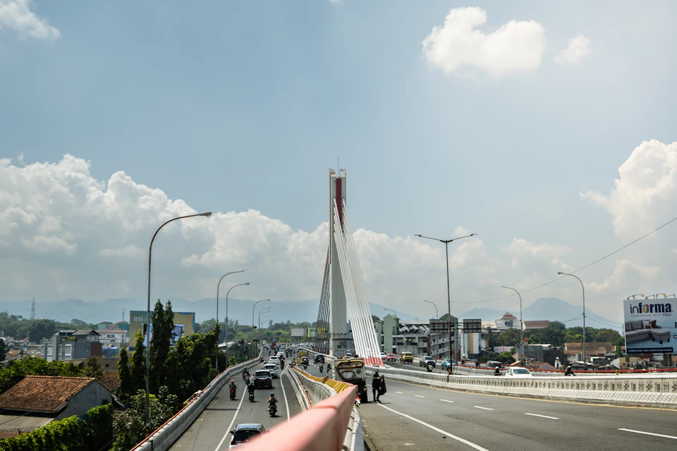 White suspension bridge spans highway, connecting two city parts separated by a river