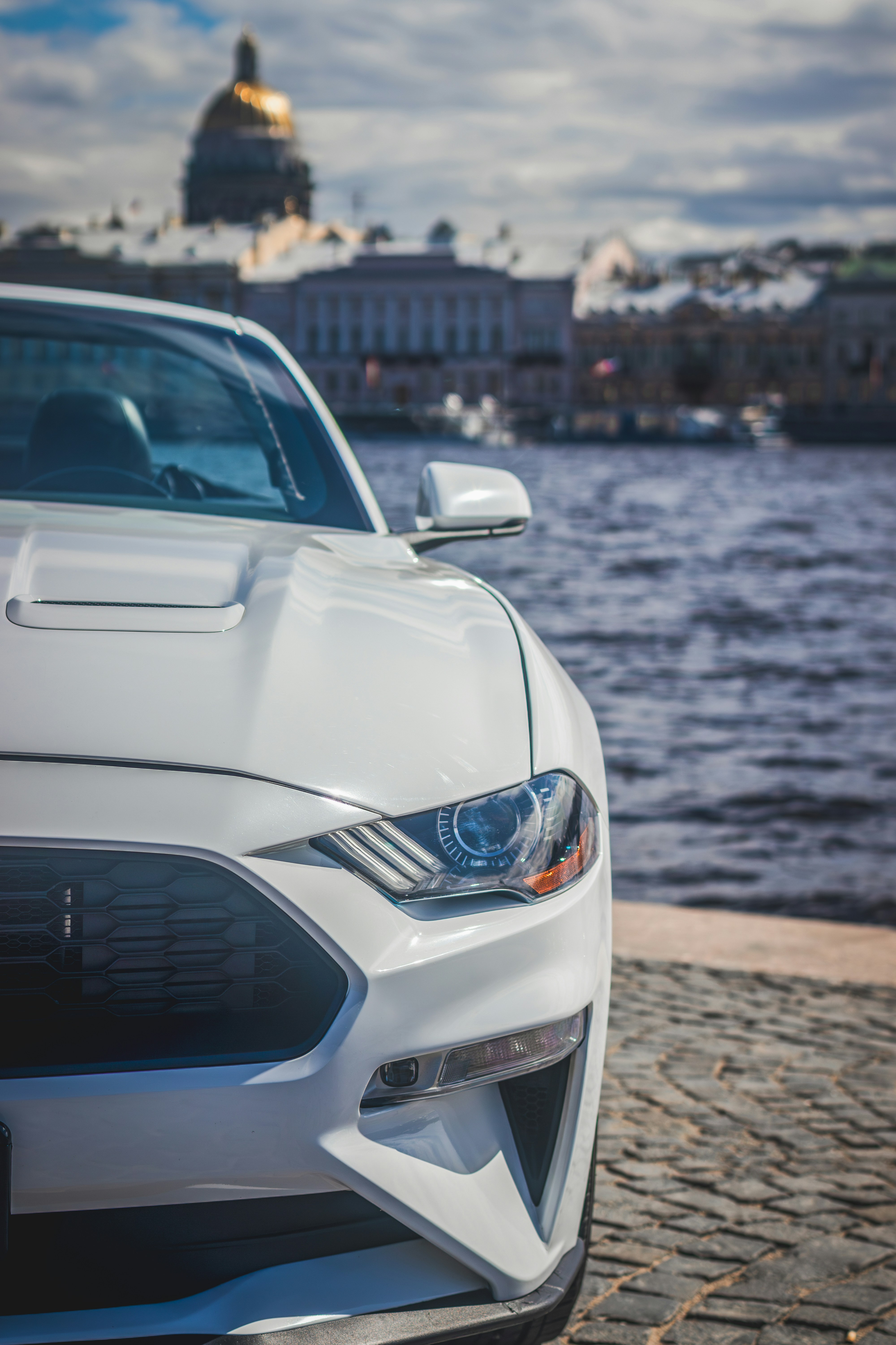 A white mustang parked near the water.