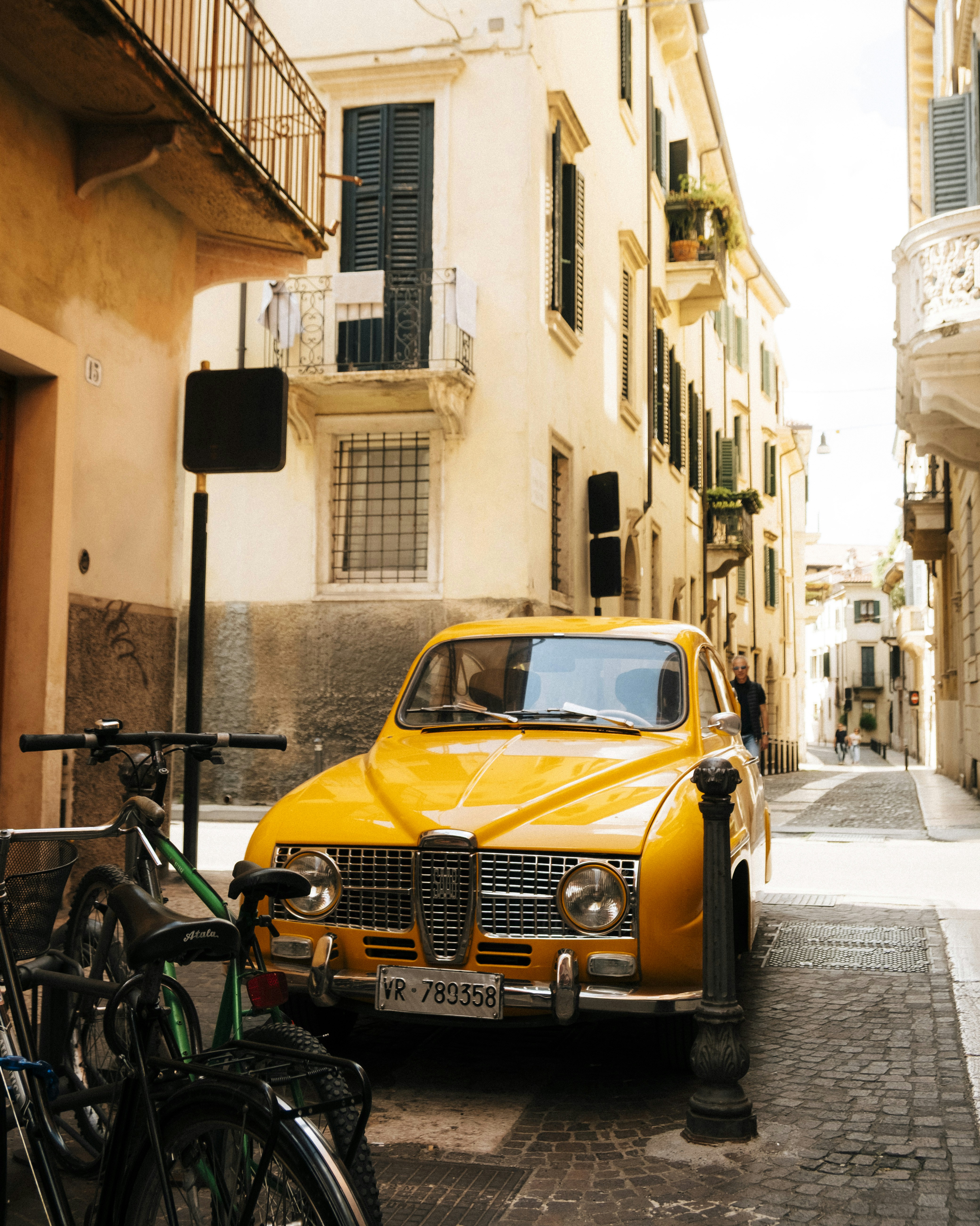 A yellow vintage car is parked in a narrow street