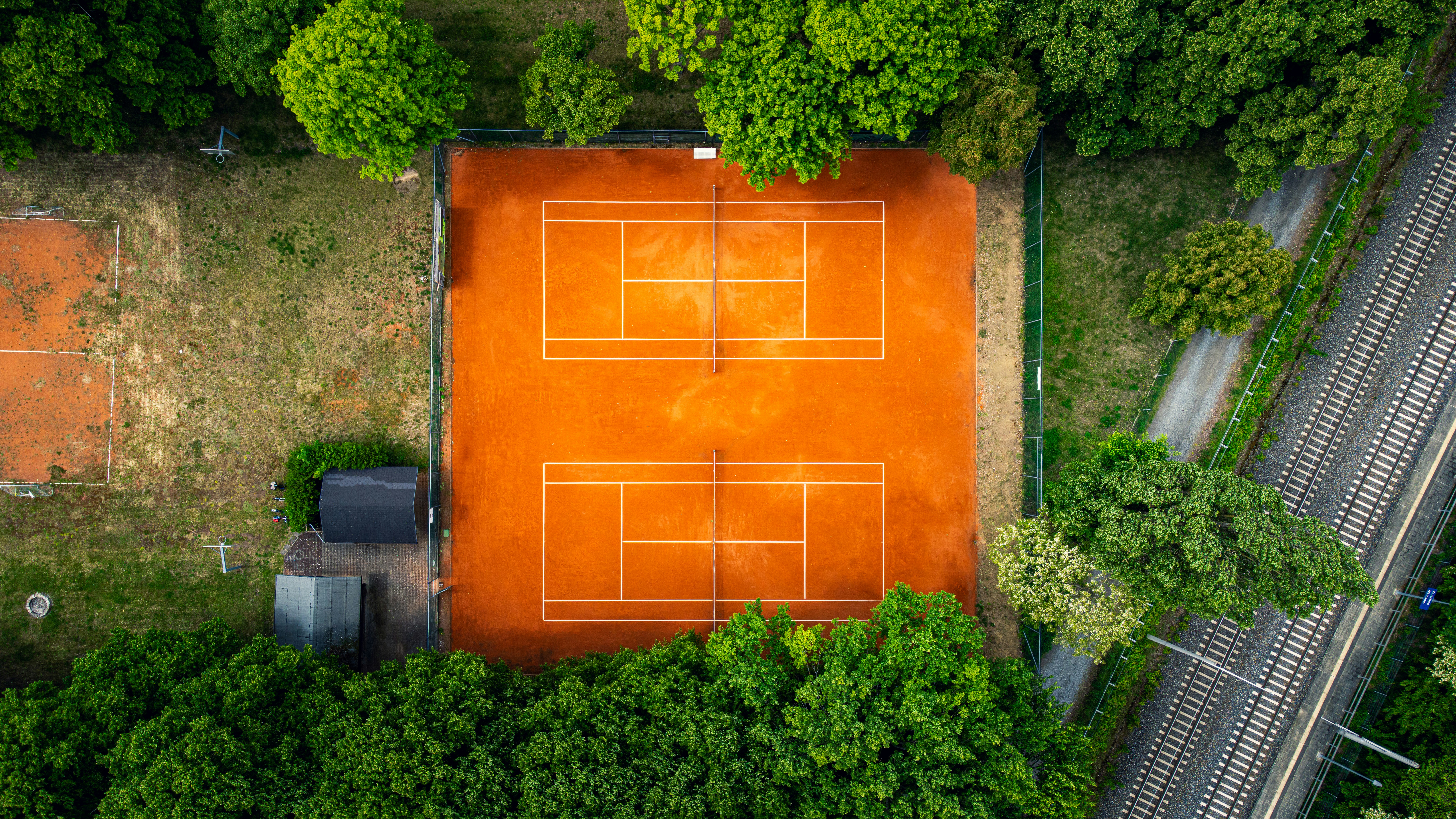Aerial view shows two tennis courts amidst trees.