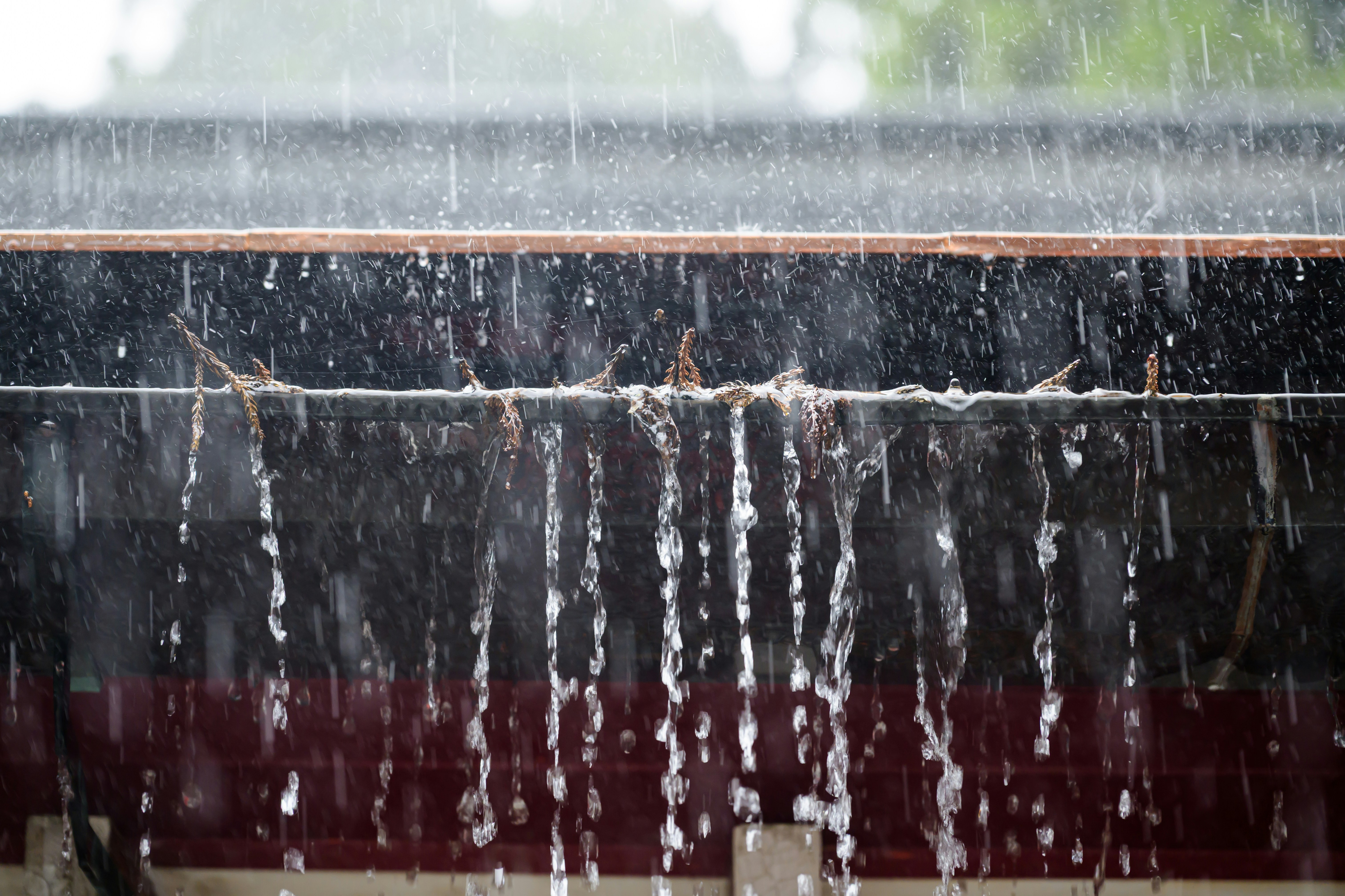 Water cascading off a roof without gutters during a storm - gutter systems and why they matter for your roof