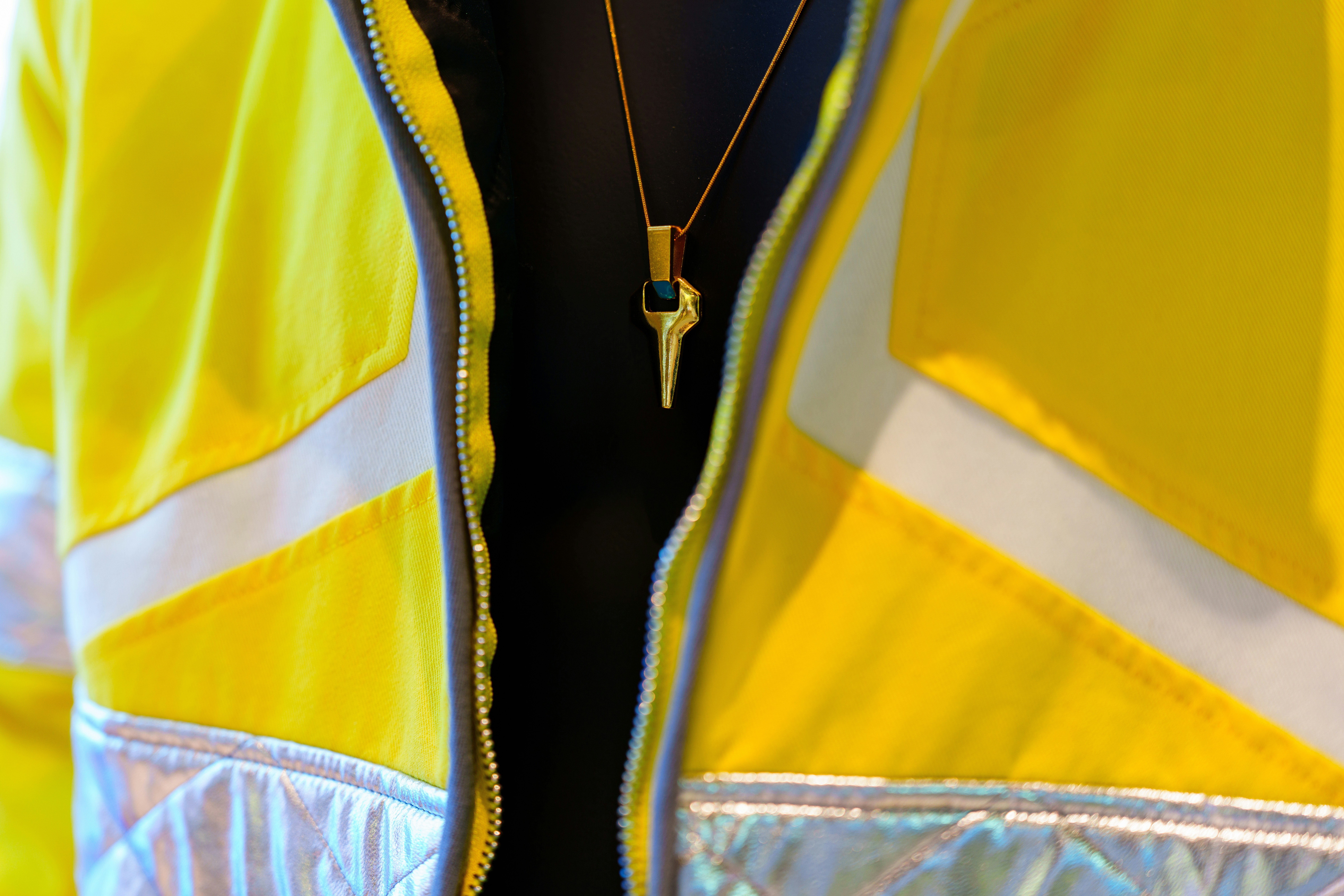 A gold necklace worn over a yellow jacket.