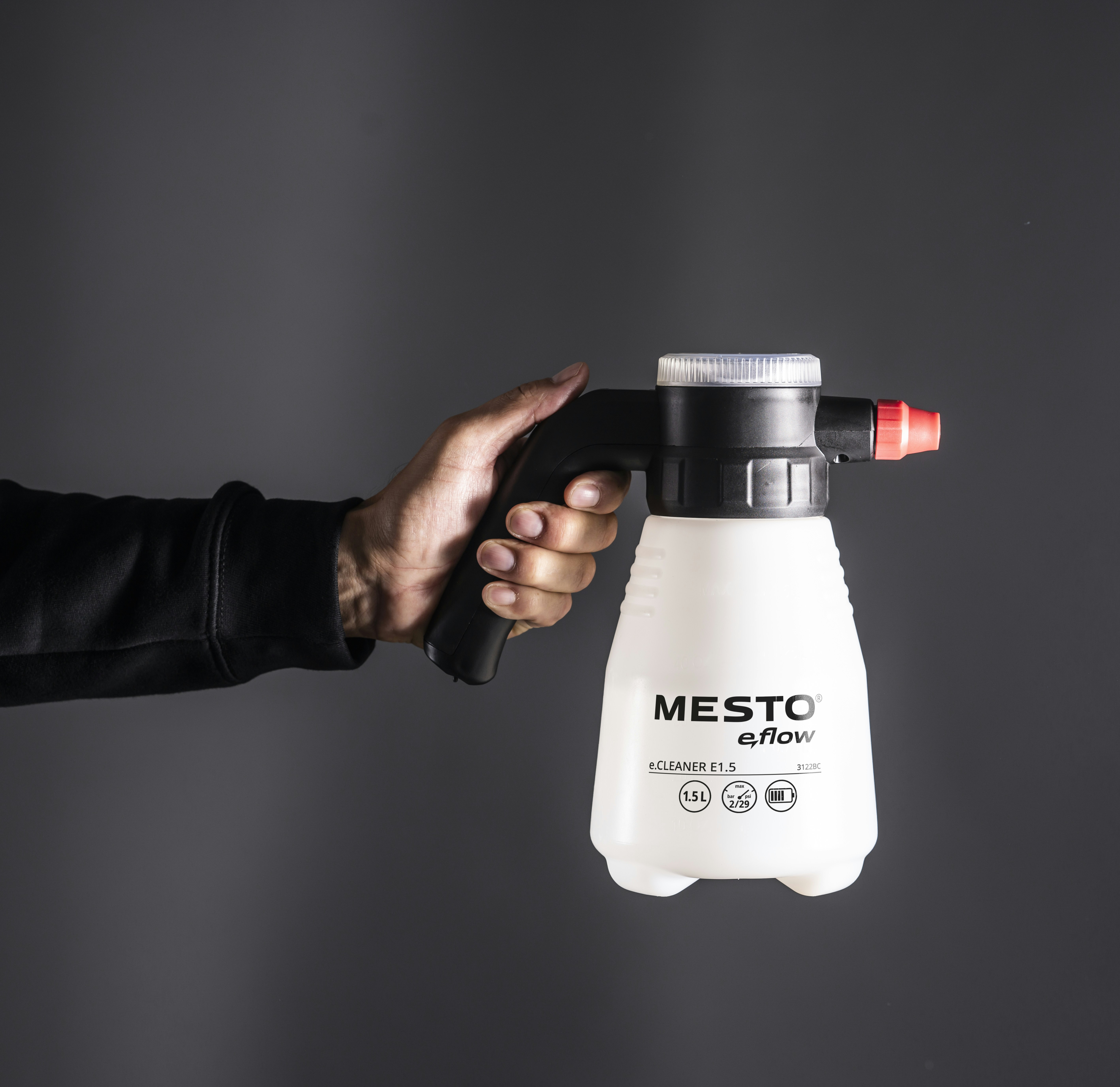 A hand holds a spray bottle against a gray backdrop.