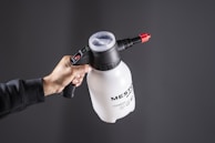 A hand holds a white pump sprayer.