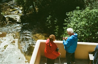 Two people watch a river from a balcony.