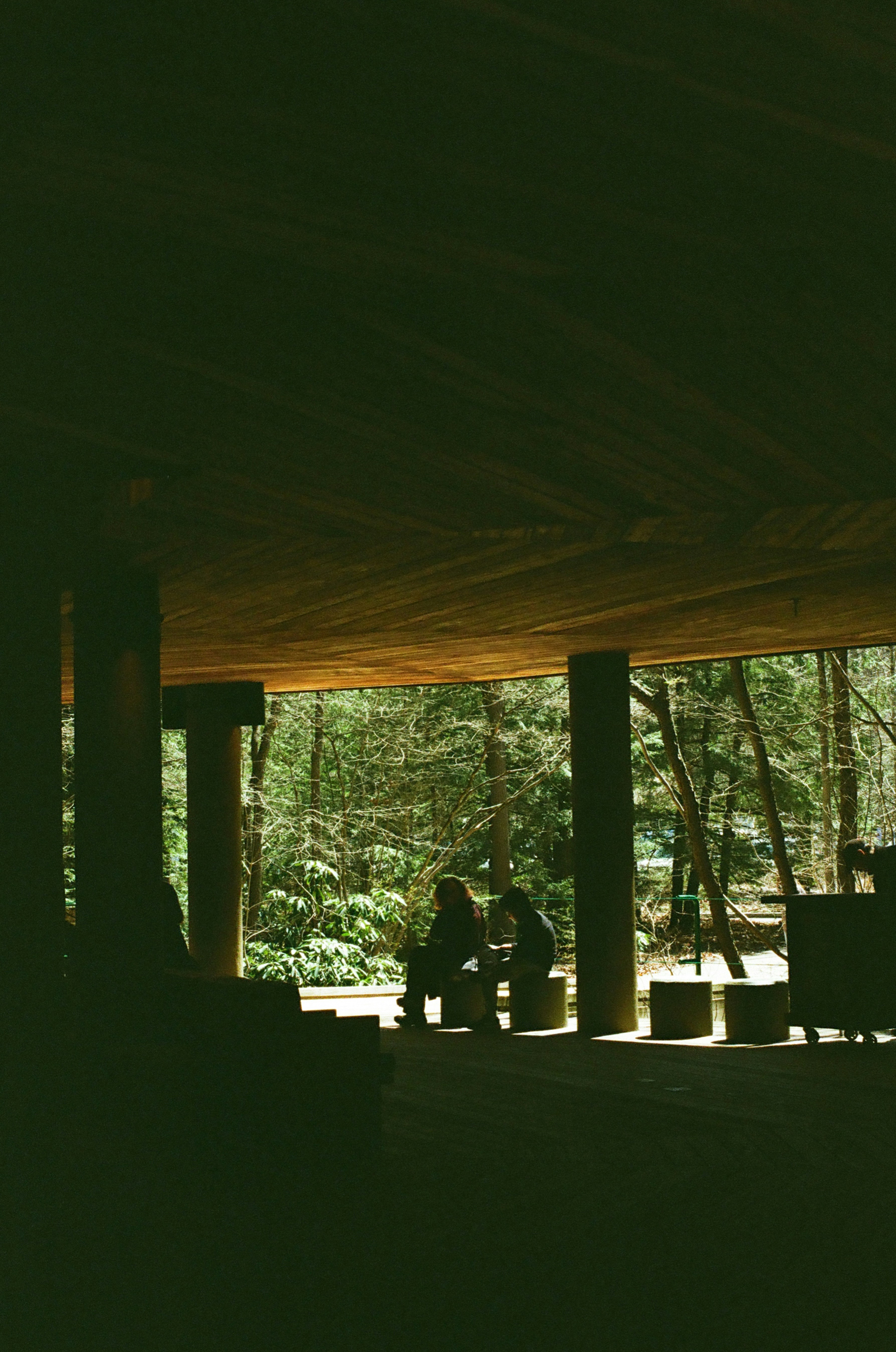 Two people sit under a concrete structure.