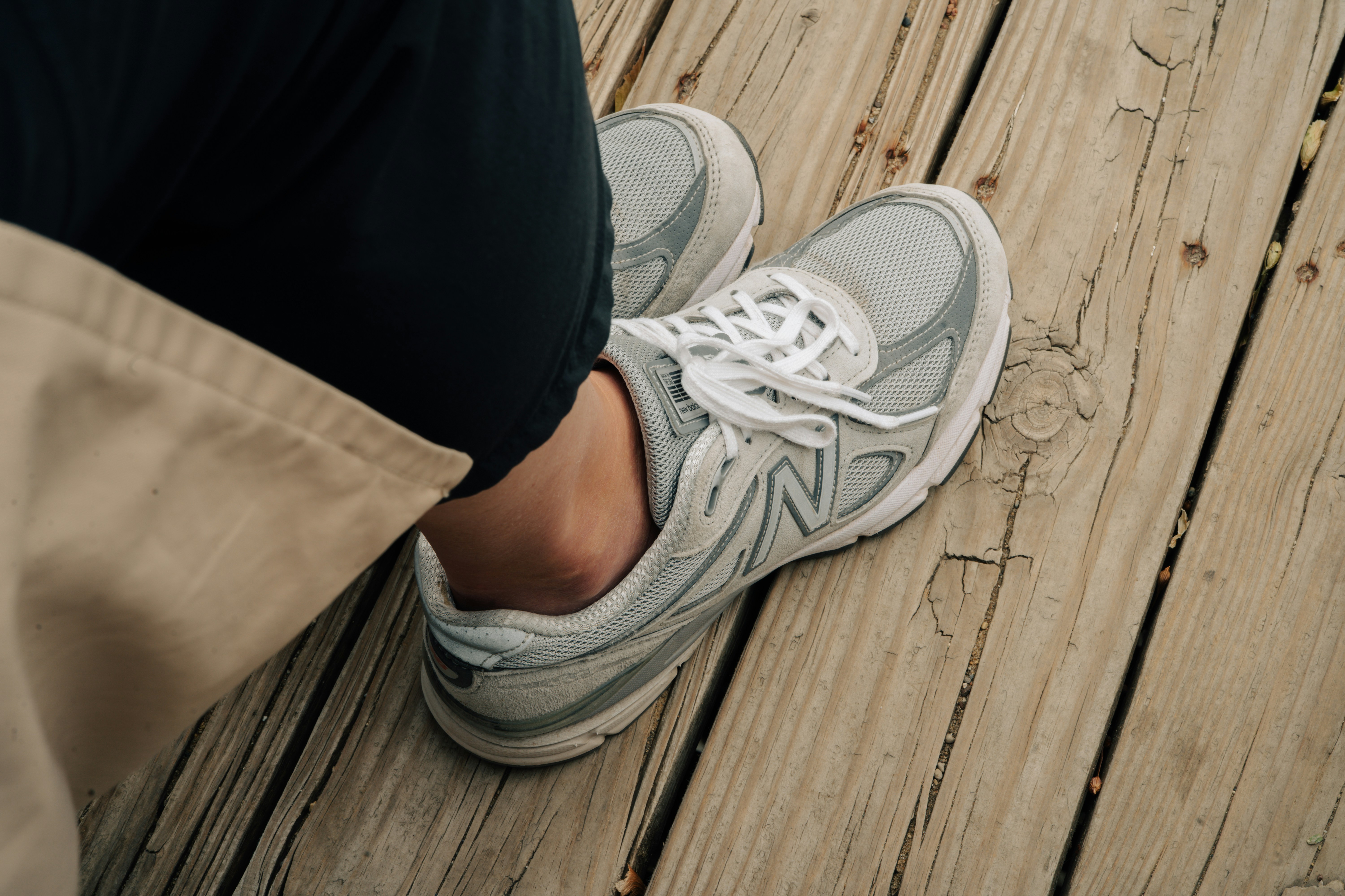 Person wears new balance sneakers on wooden planks.