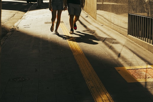Two people are walking down a sunlit, shaded street.