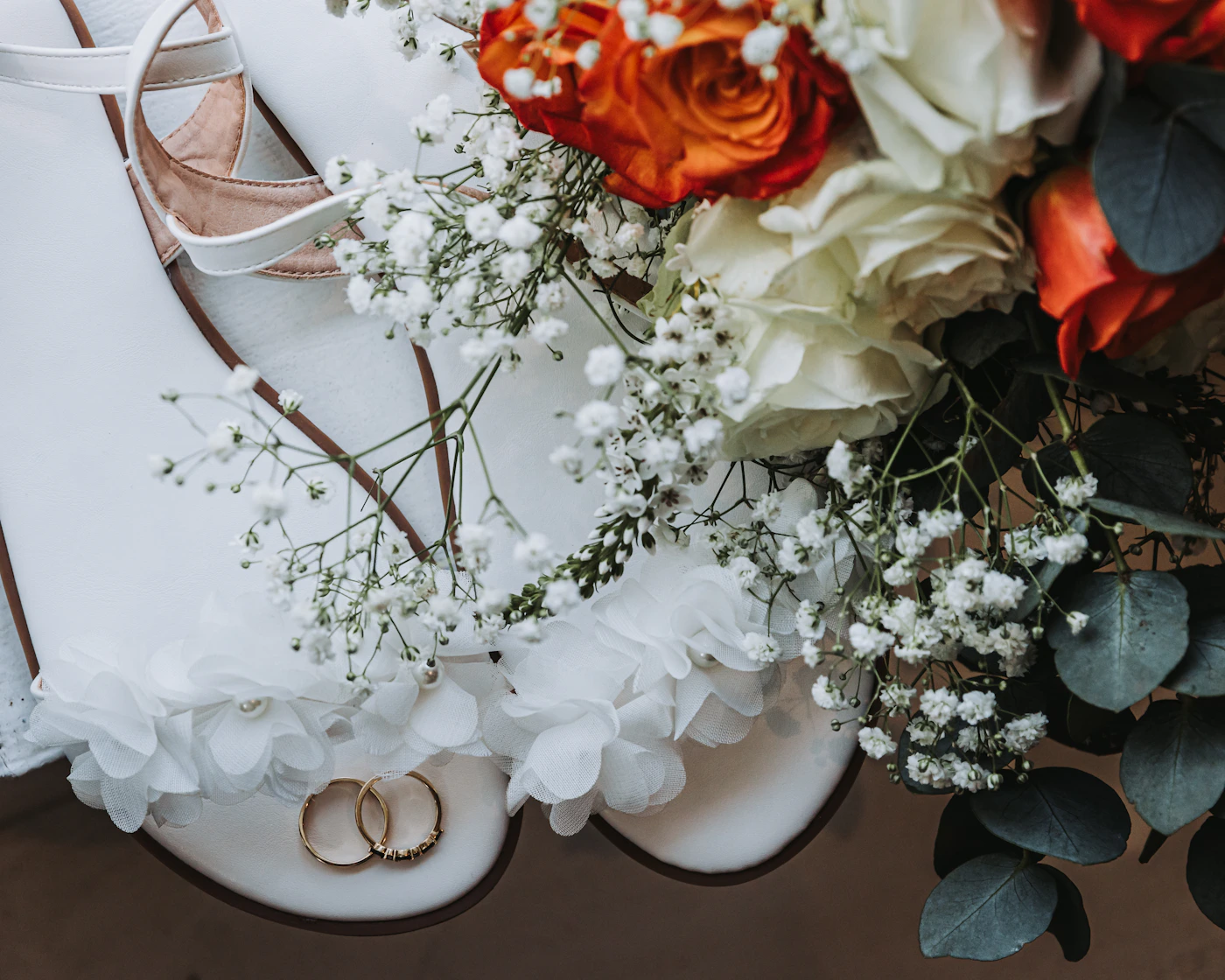 Wedding shoes rings and flowers arranged as a flat lay detail photograph showing the getting ready detail work that documents the objects of the wedding day before the ceremony begins