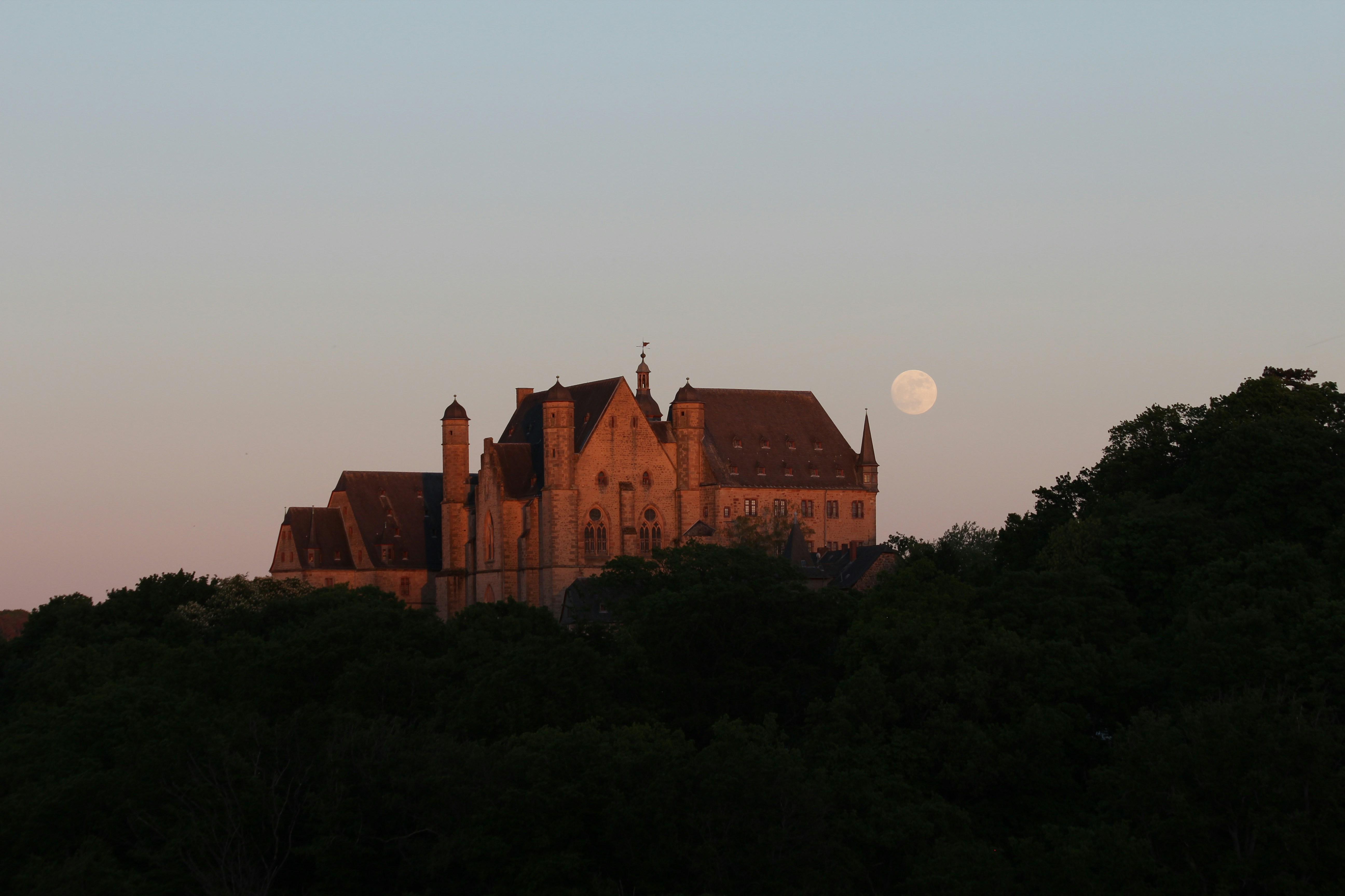 Castle silhouetted against the sunset with the moon.