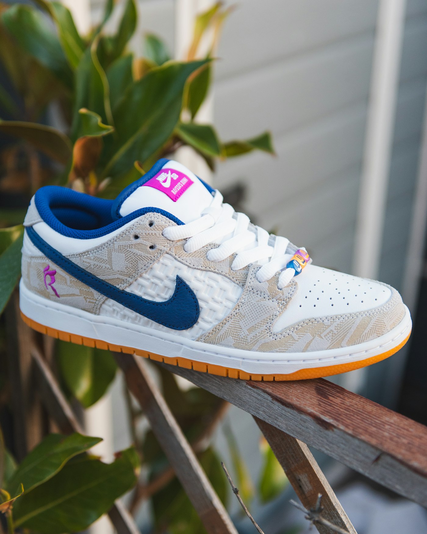 White, blue and orange Nike SB Dunk Low sneaker displayed on a rail outdoors
