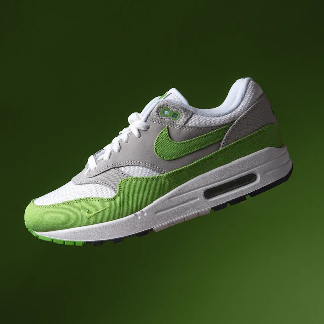 A green and white Nike Air Max 1 sneaker floating in mid air with its visible Air unit in the heel