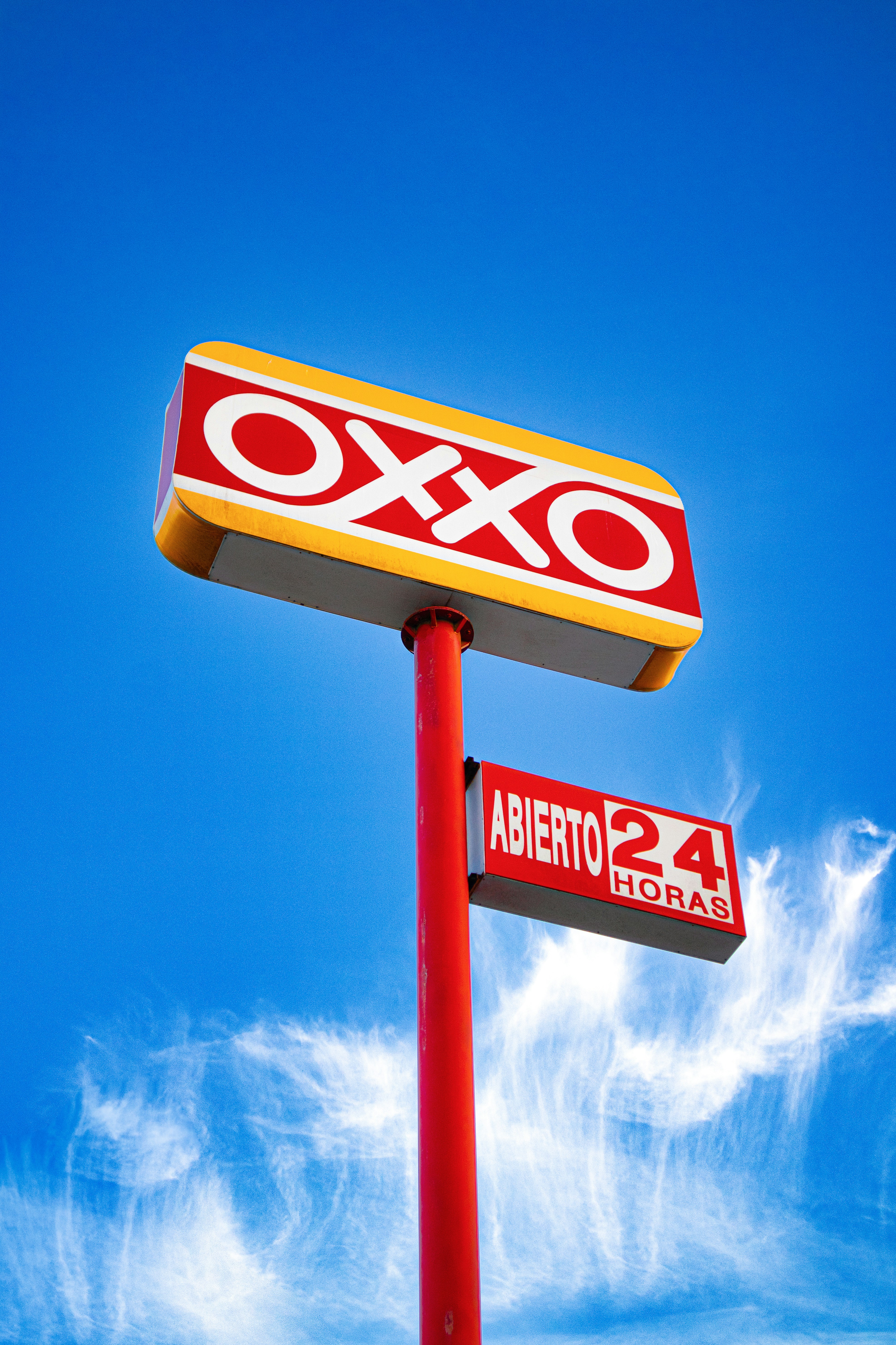 Oxxo store sign illuminated against a blue sky.