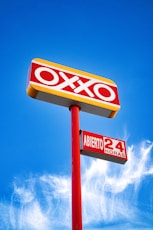 Oxxo store sign illuminated against a blue sky.