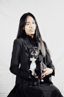Woman in black suit holds a small dog.