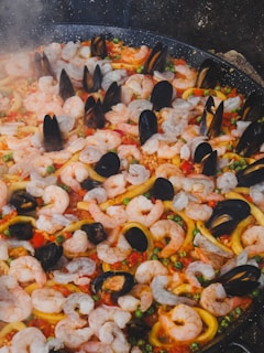 Seafood paella is cooking in a large pan.